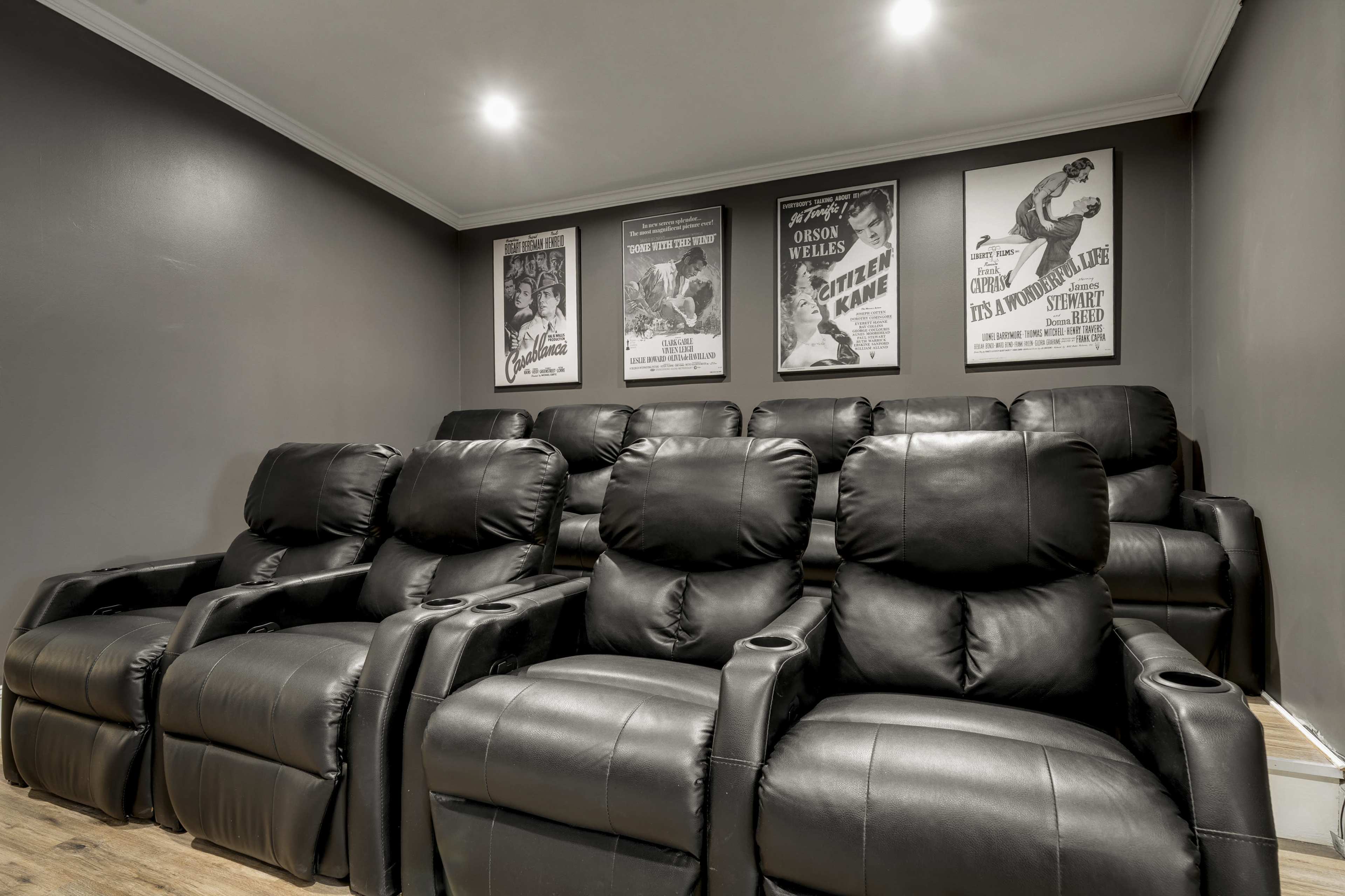 The image shows a home theater with black recliner seating arranged in a row, complemented by vintage movie posters on the wall.
