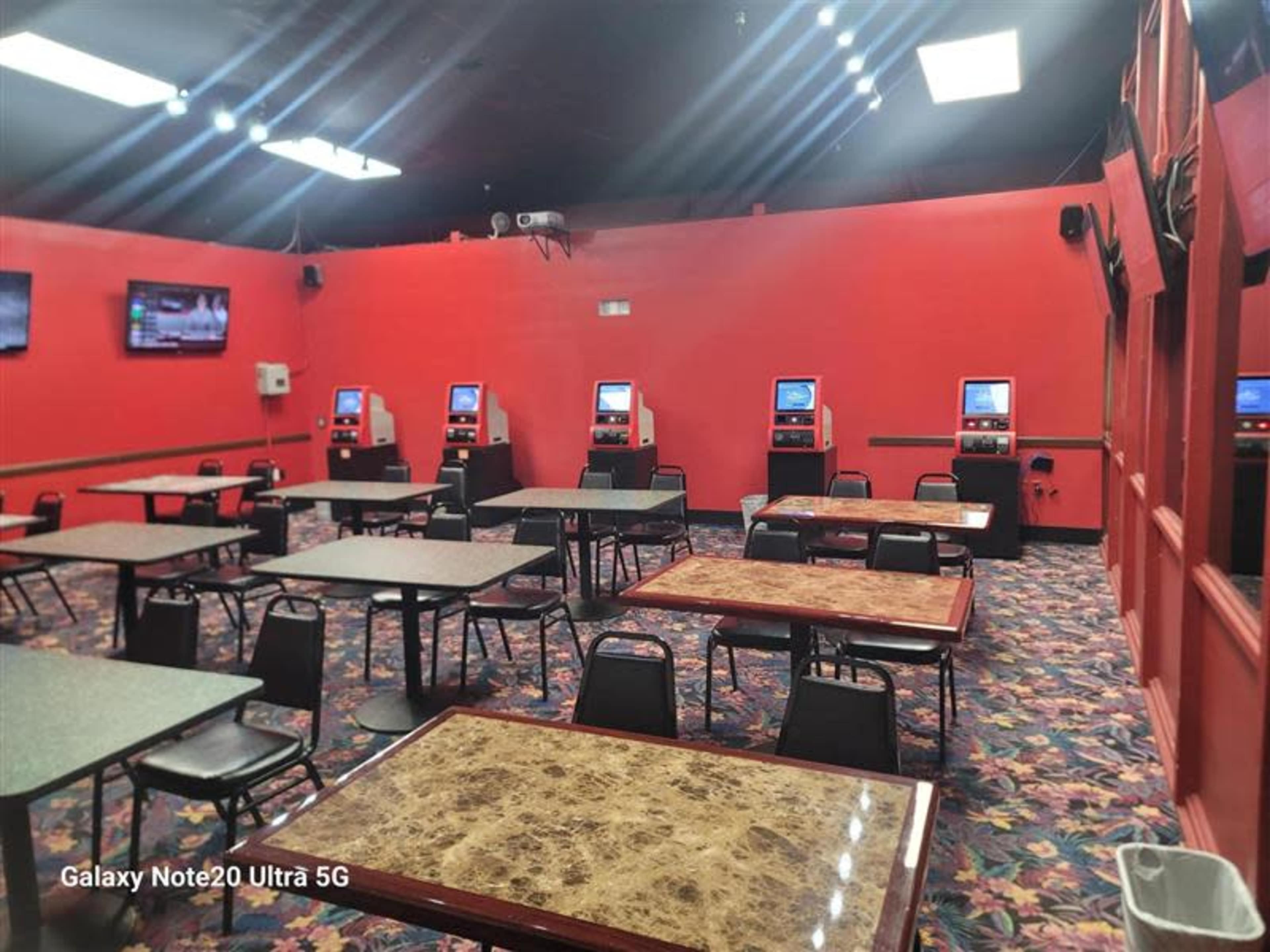 The image shows a brightly colored red room with several tables and four gaming machines lined against the wall.