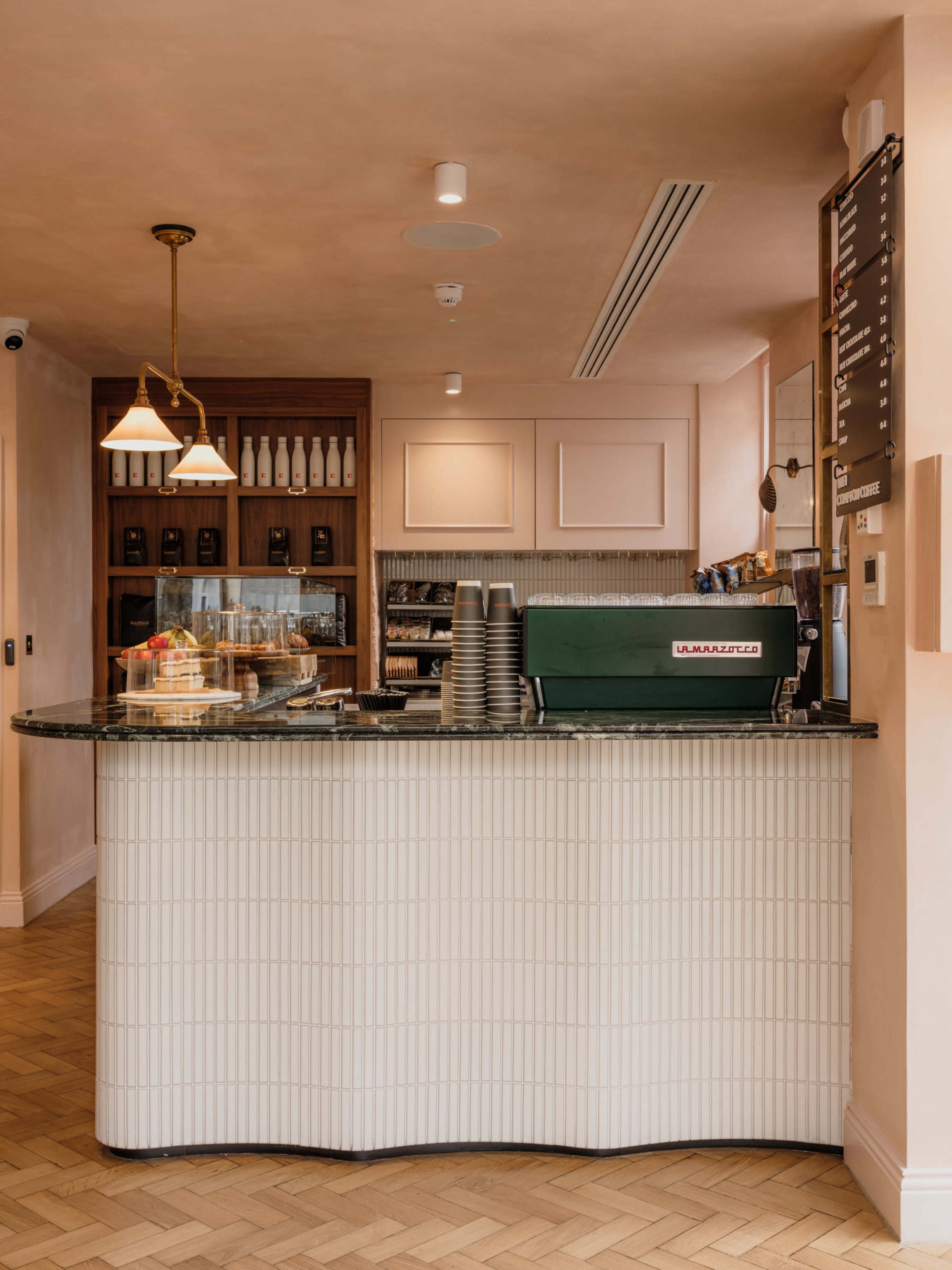 A modern café interior with a streamlined service counter, featuring a green espresso machine and a display case with pastries.