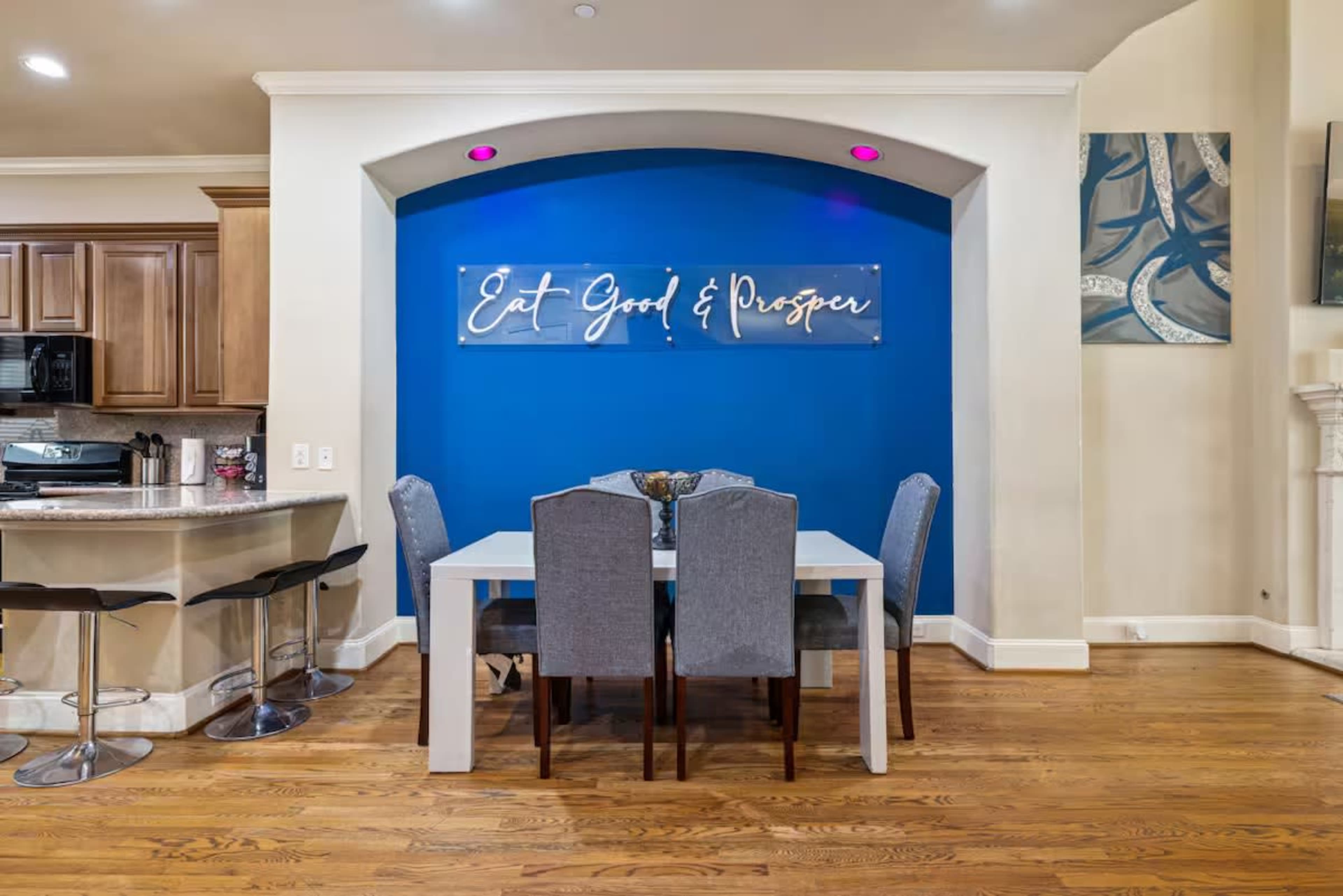 A dining area features a table surrounded by gray chairs, set against a blue accent wall with a clear sign that reads "Eat Good & Prosper."