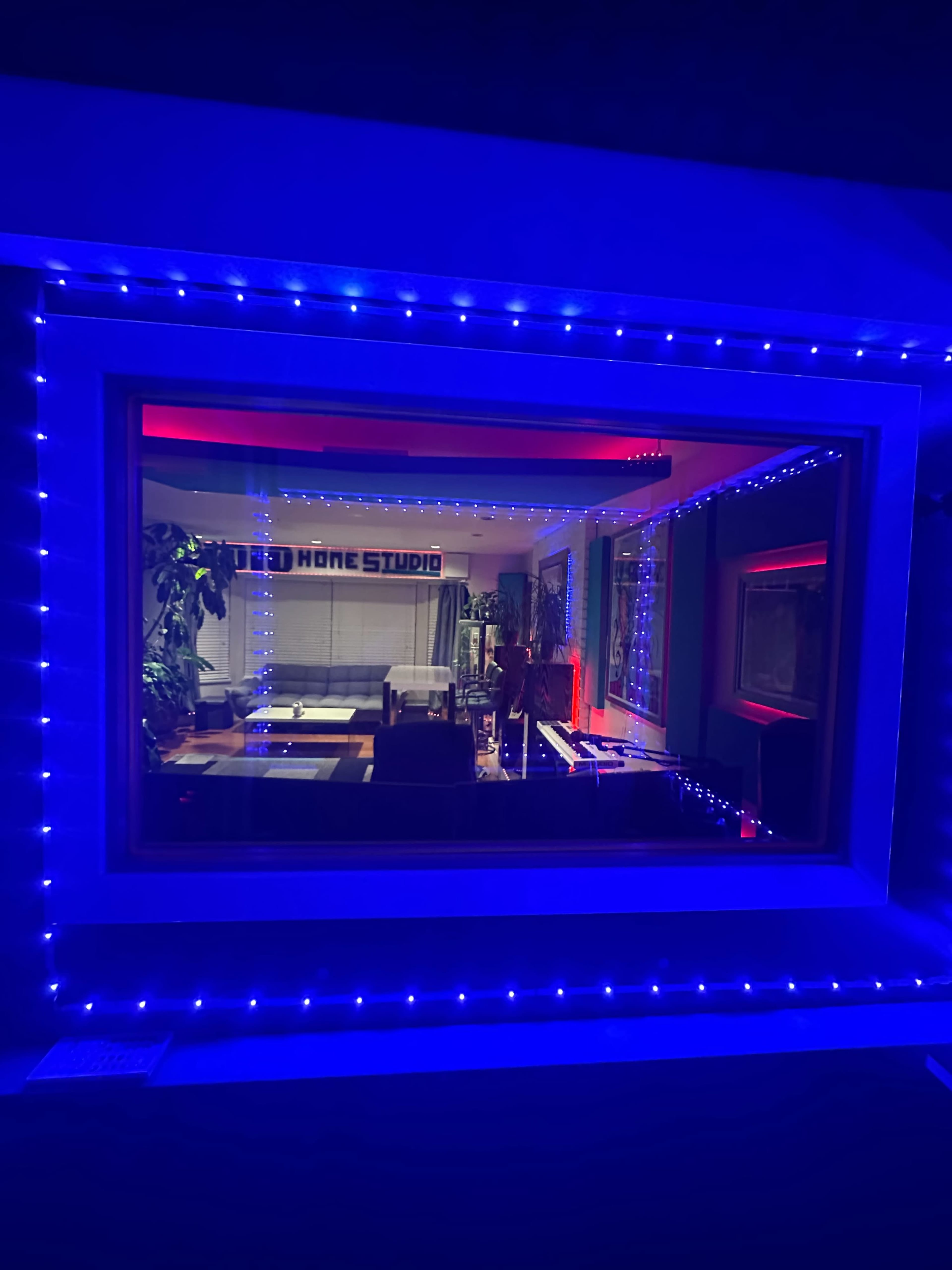A brightly lit home studio with colorful LED lights framing a window, revealing a modern interior setup.
