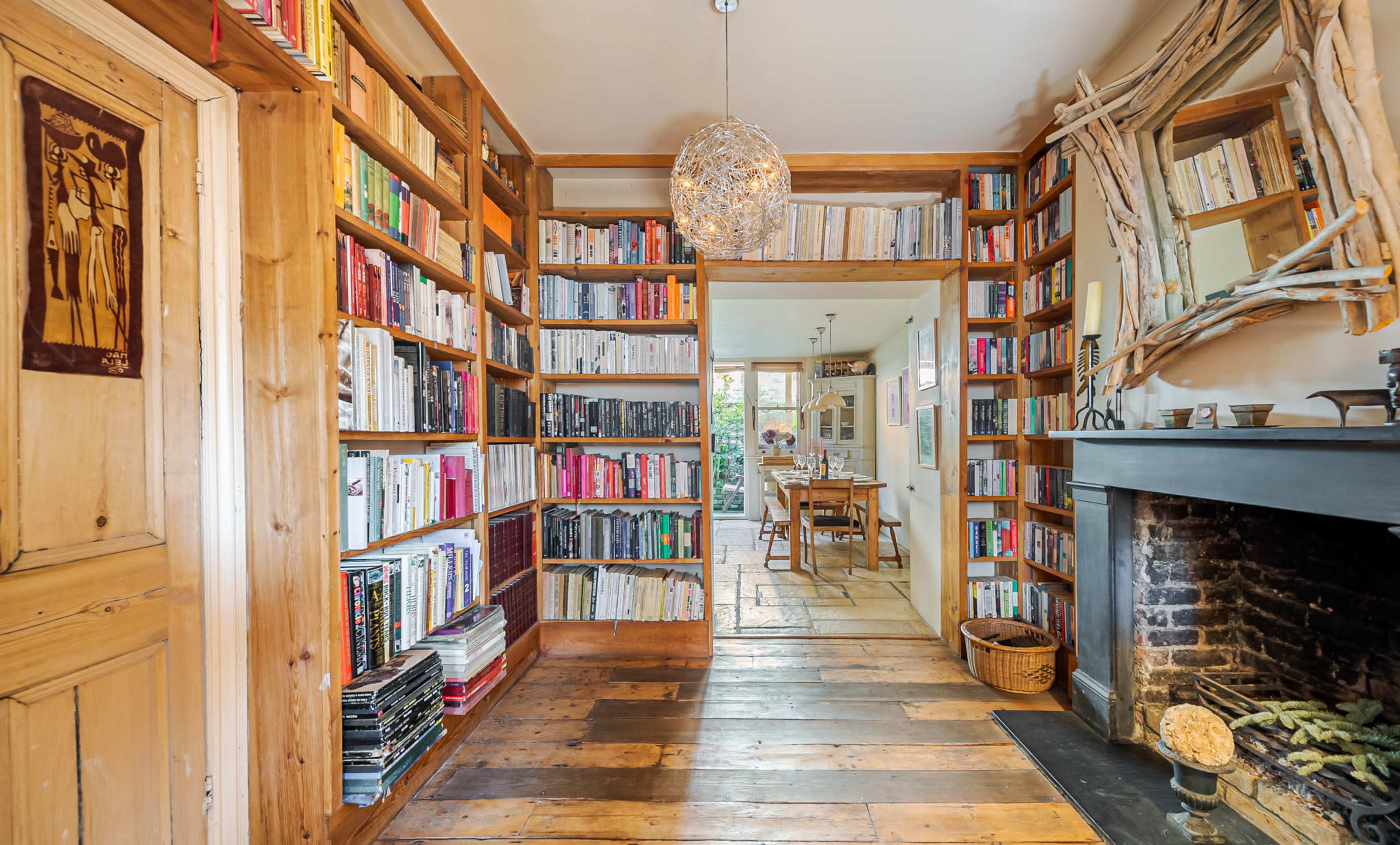 A cozy room features bookshelves filled with colorful books, a wooden floor, and a fireplace.