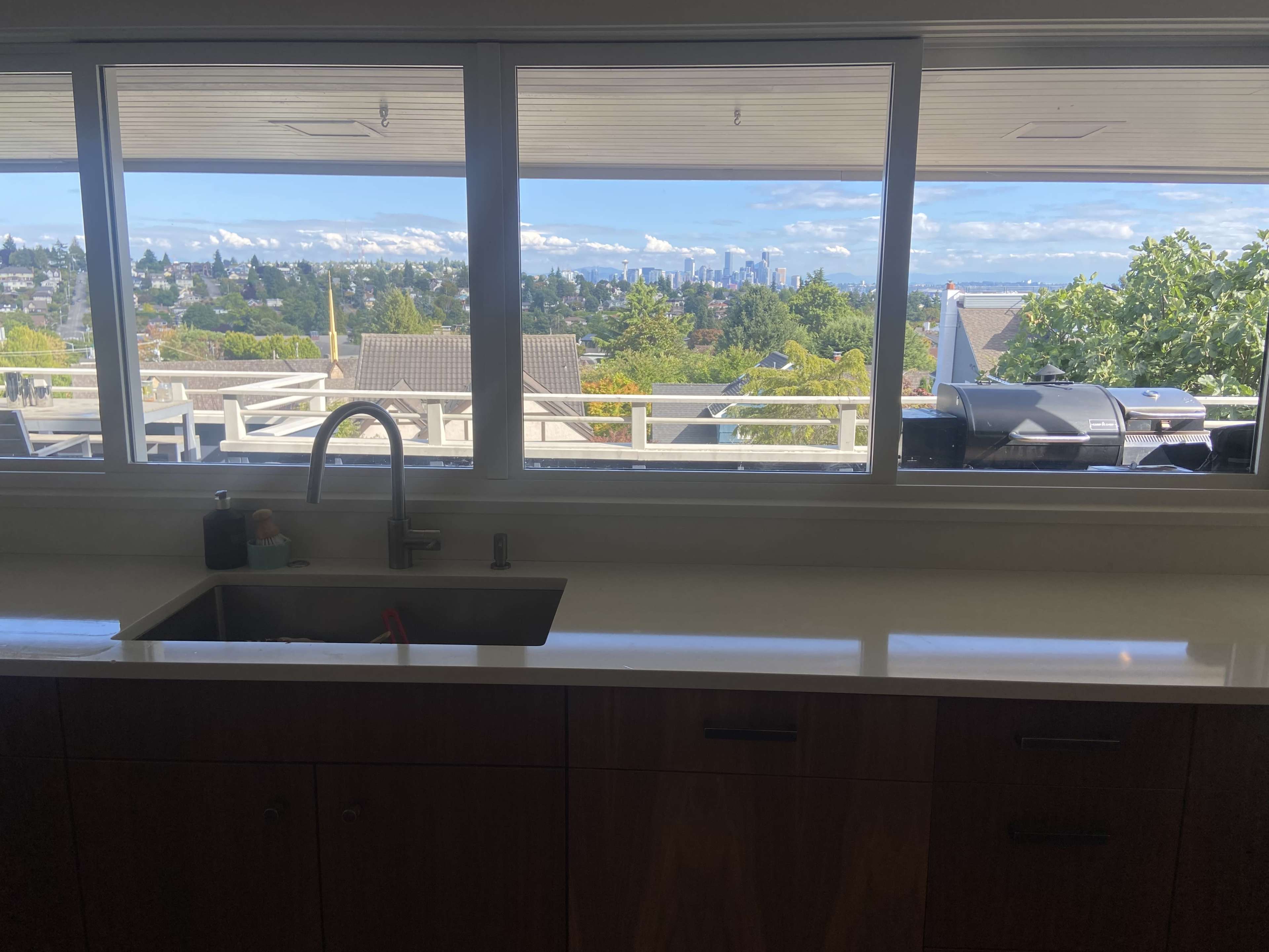 A kitchen sink with a view of a city skyline through large windows surrounded by greenery.