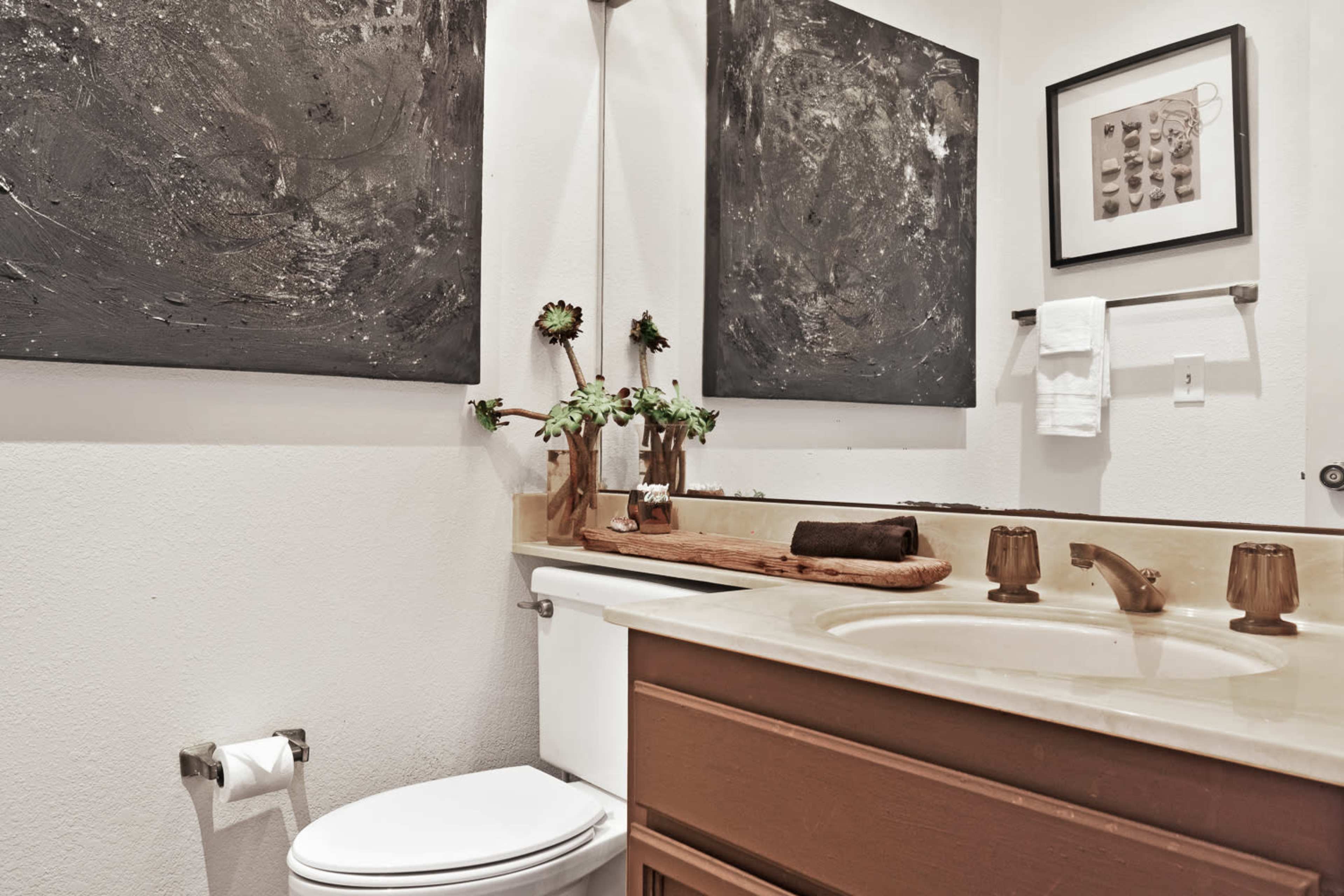 A compact bathroom featuring a toilet, a sink with a countertop, and two large abstract paintings on the walls.