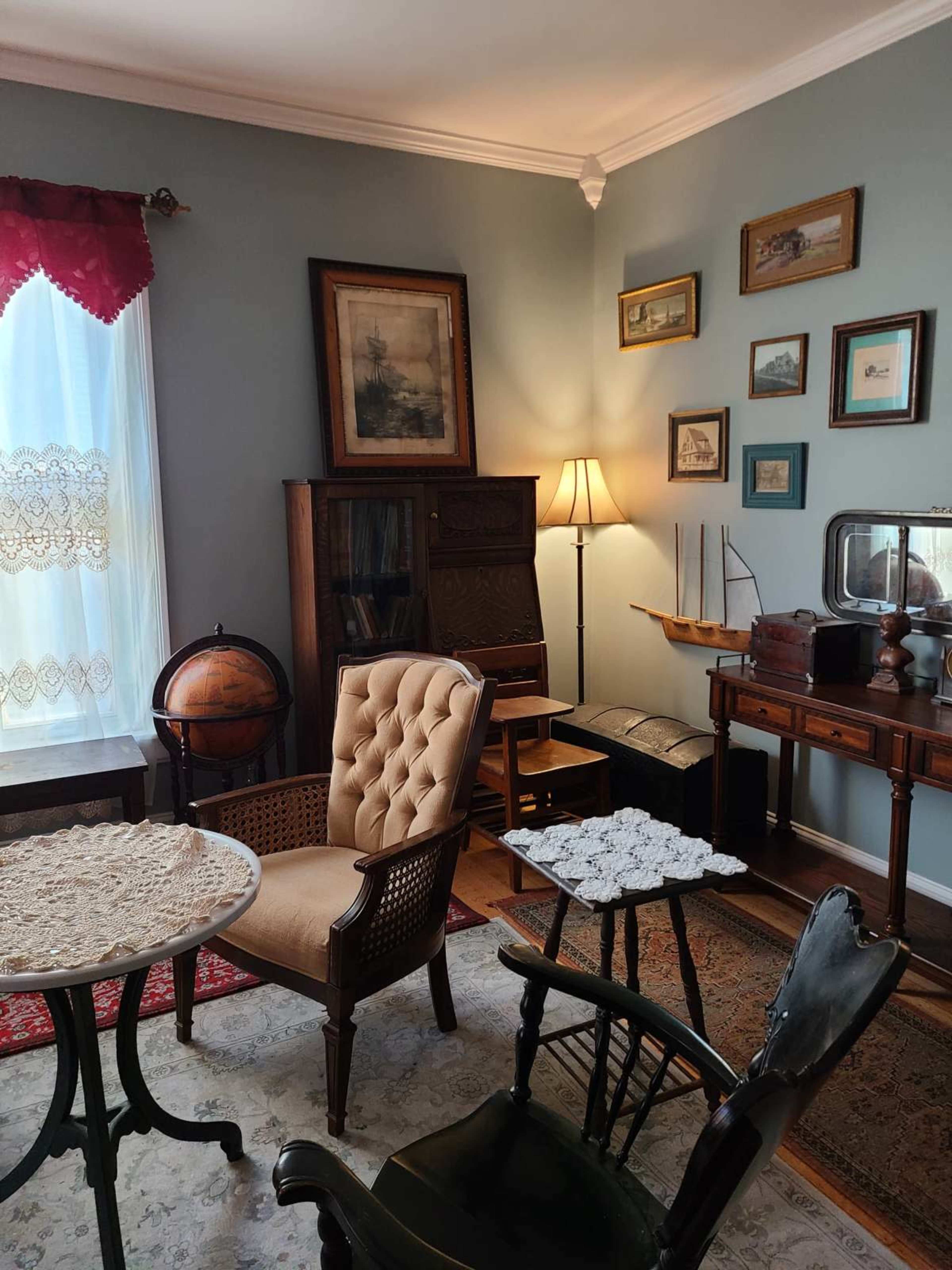 A cozy sitting area with vintage furniture, including a brown upholstered chair, a wooden globe stand, a small round table, and framed artwork on the walls.
