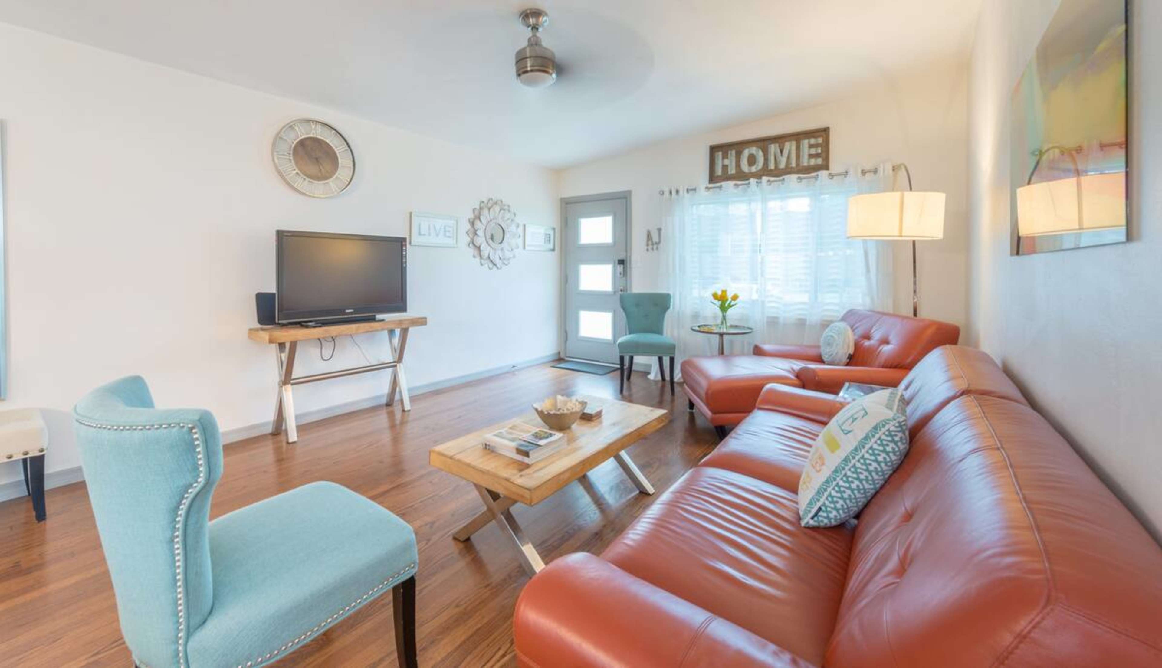 A cozy living room with a television, two orange sofas, a wooden coffee table, and a light blue chair, all arranged around a door with a window.