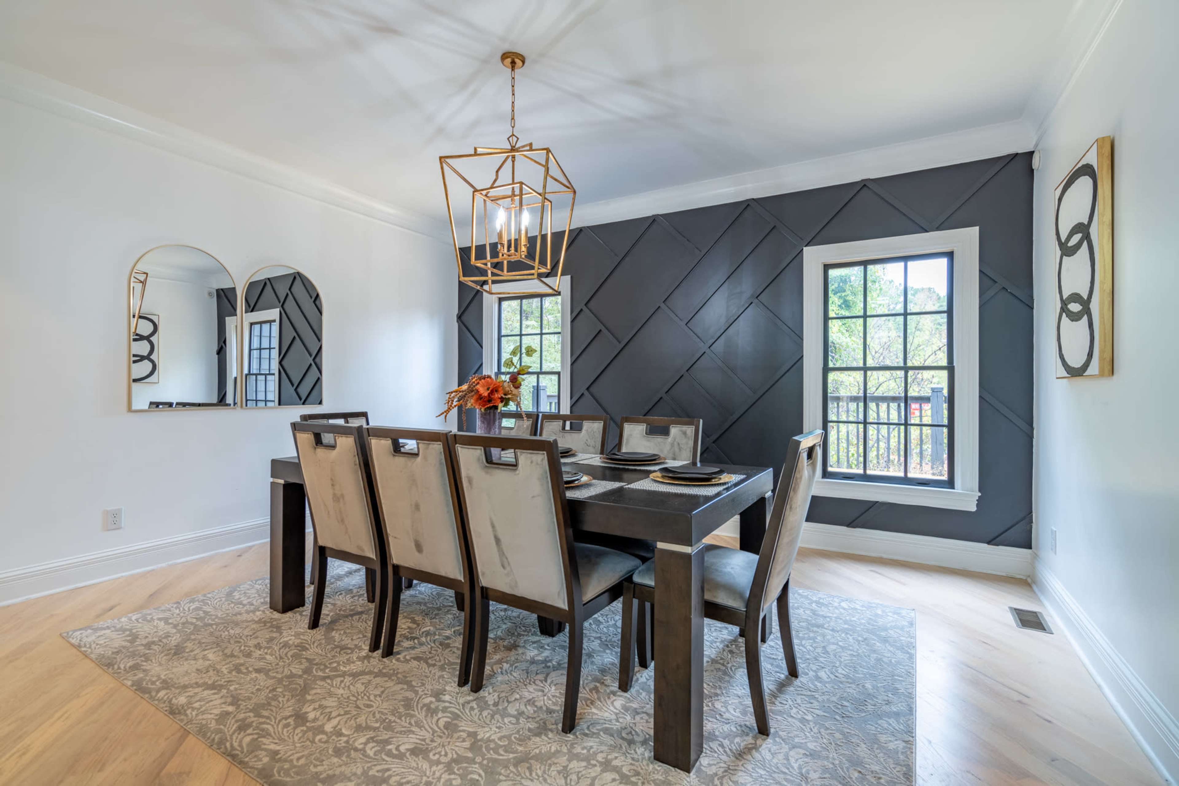 A dining room with a rectangular table surrounded by six chairs, featuring a stylish light fixture and a textured accent wall.