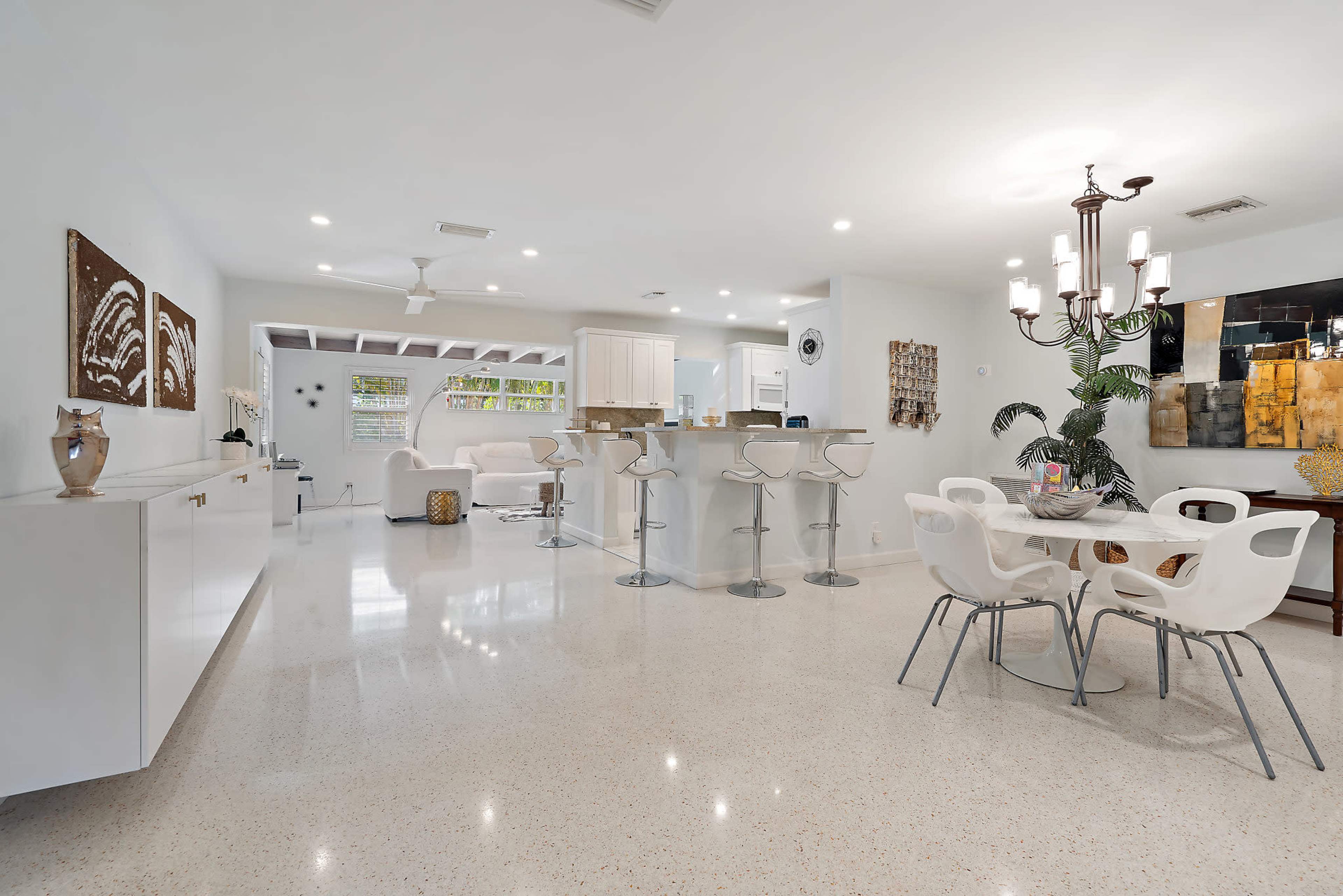A modern open-concept living area with a white kitchen, bar seating, and a dining table.