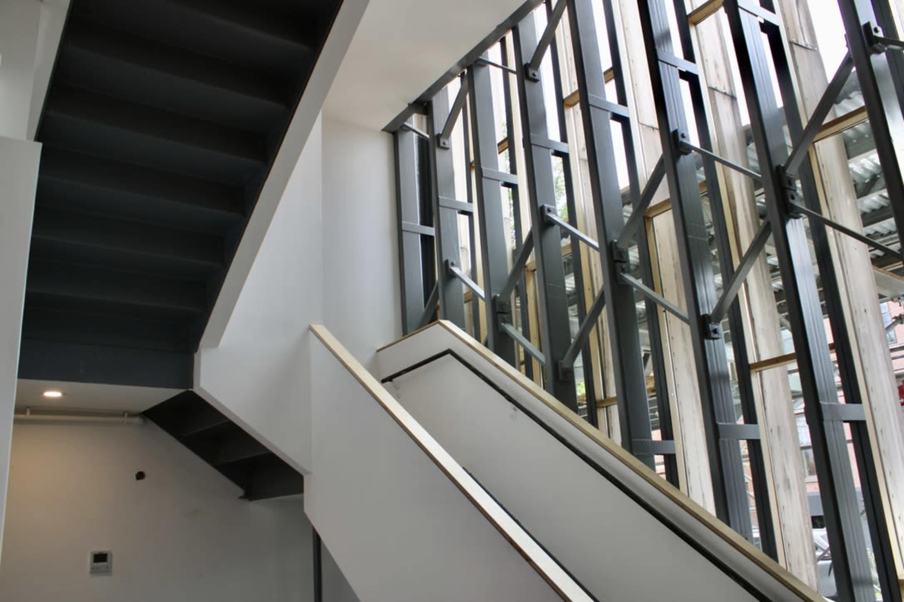The image shows a stairwell with a dark staircase and a large glass wall featuring structural supports.