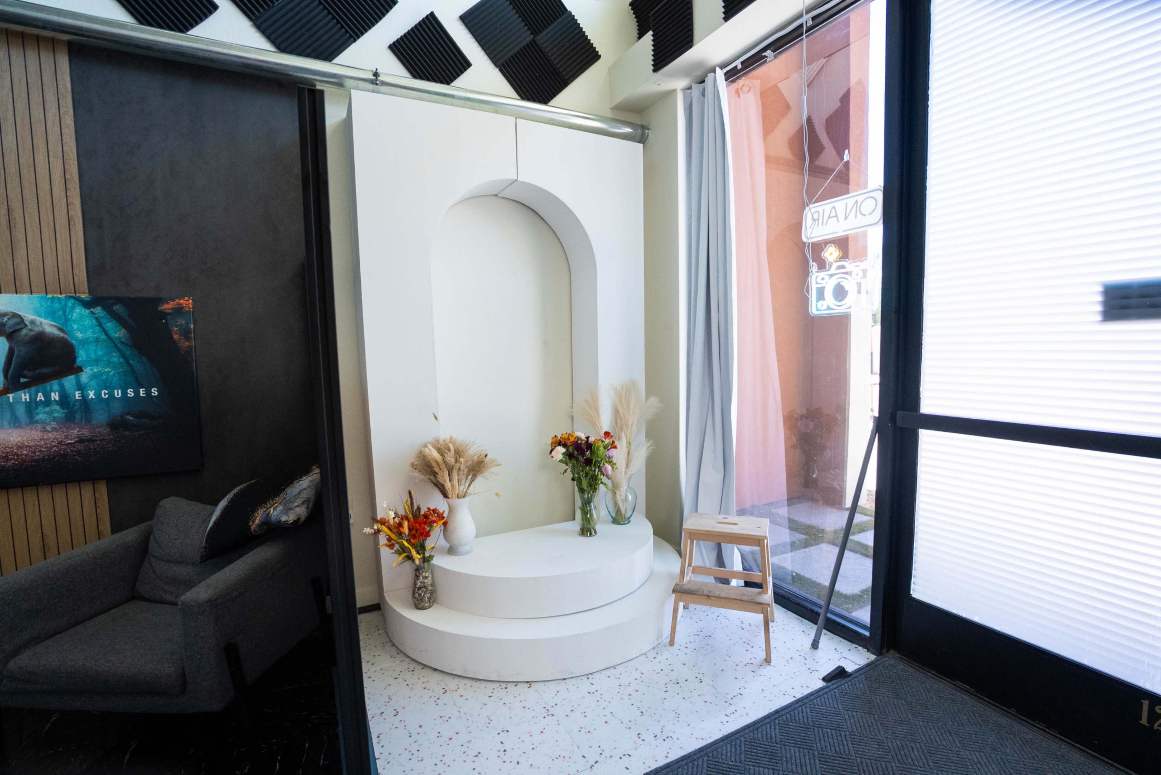 The image shows a modern interior space featuring a circular podium with decorative flowers and a small stool, adjacent to a seating area and large glass entrance.