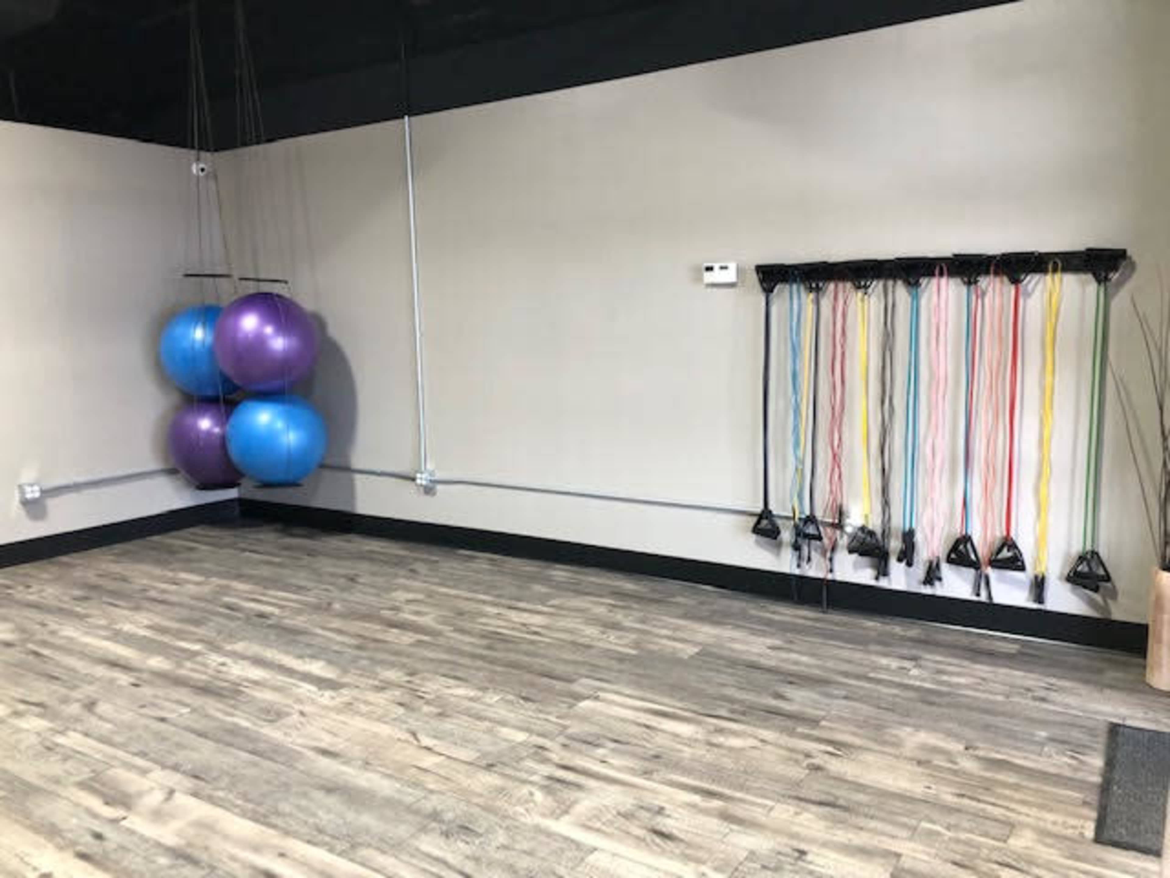 The image shows a fitness studio with two purple exercise balls and a set of resistance bands mounted on the wall.