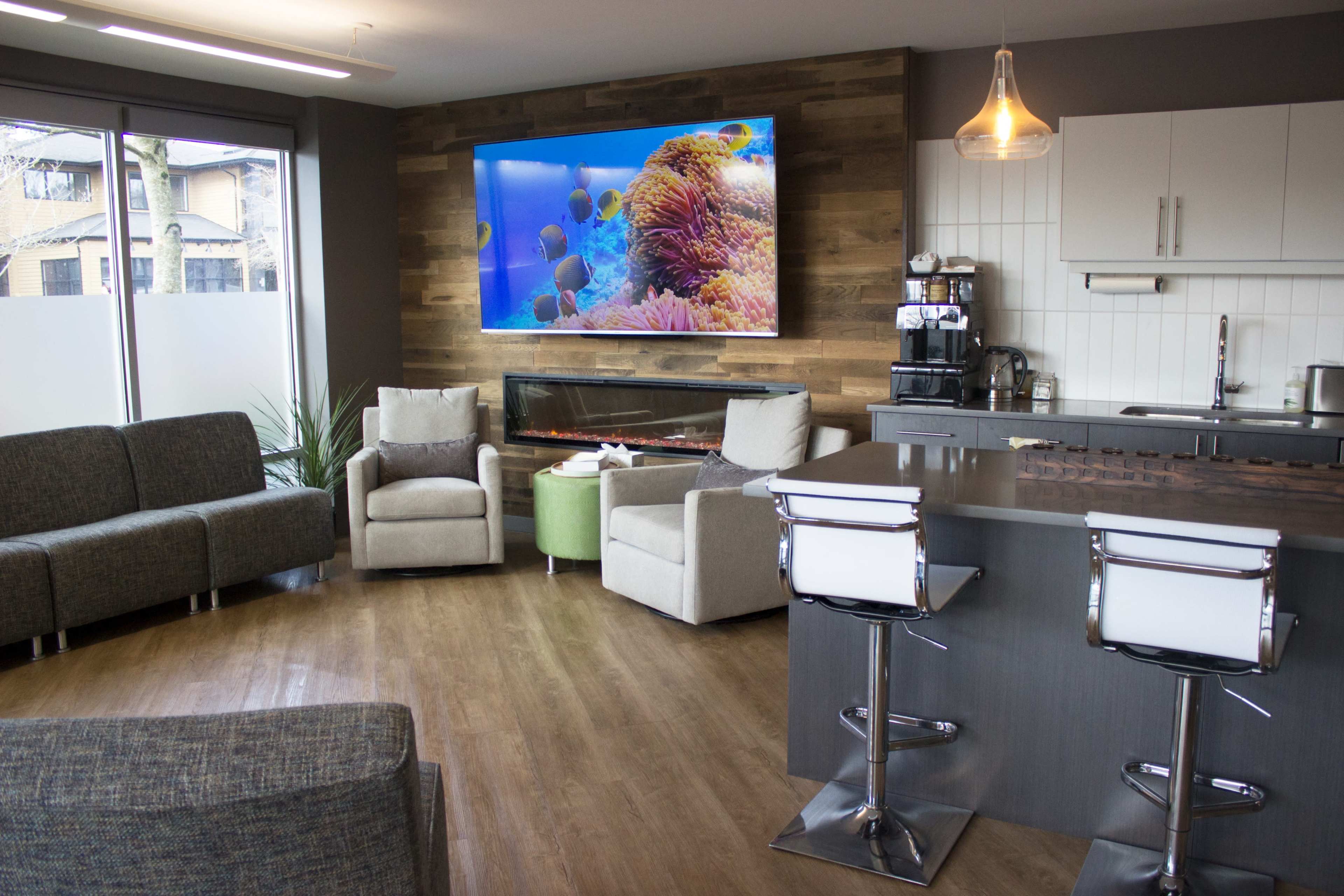A modern living space featuring a kitchen, seating area with couches and chairs, and a large television displaying an underwater scene.
