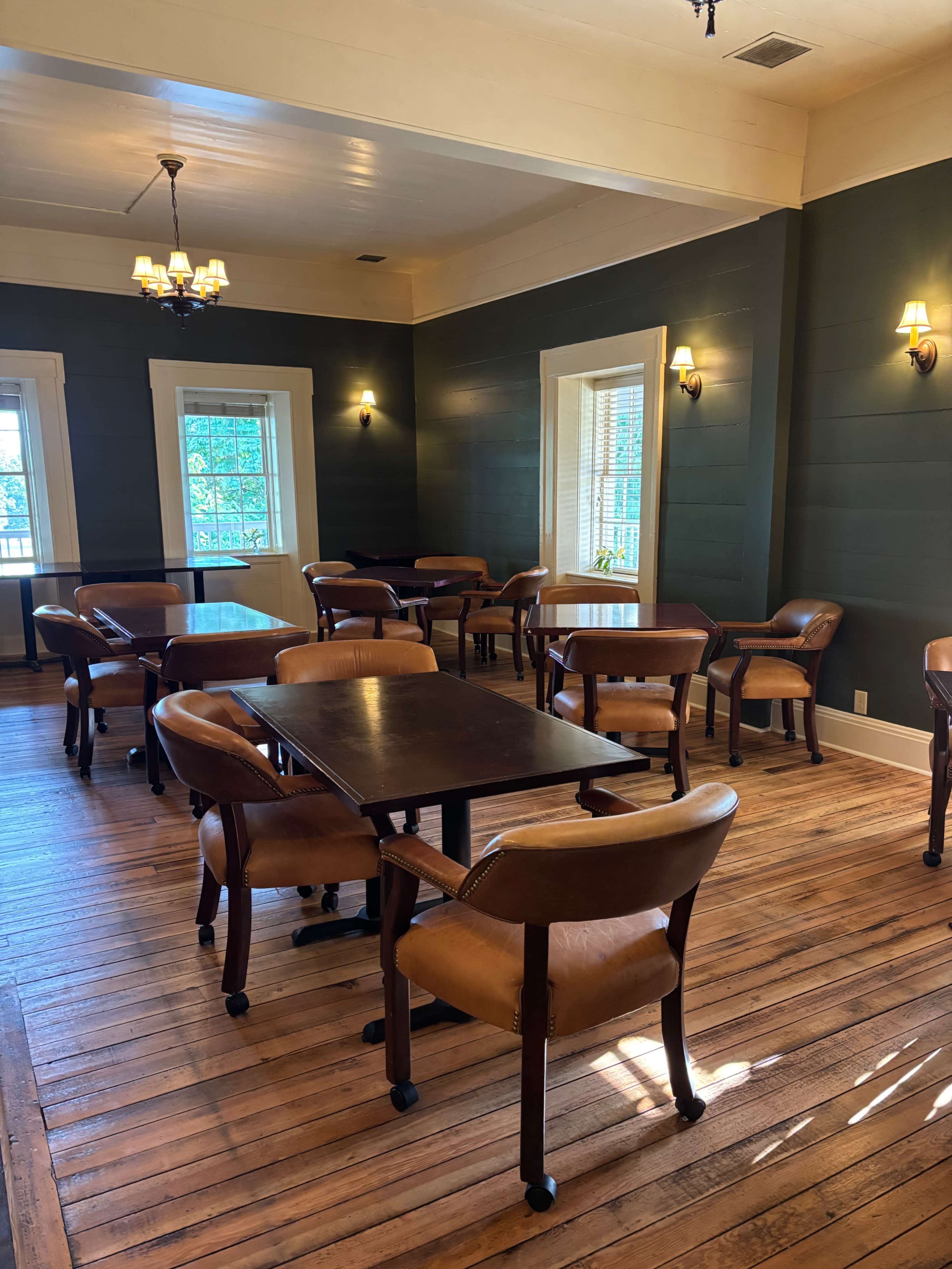 The image shows a well-lit dining room with wooden tables and chairs arranged neatly on a polished wooden floor.