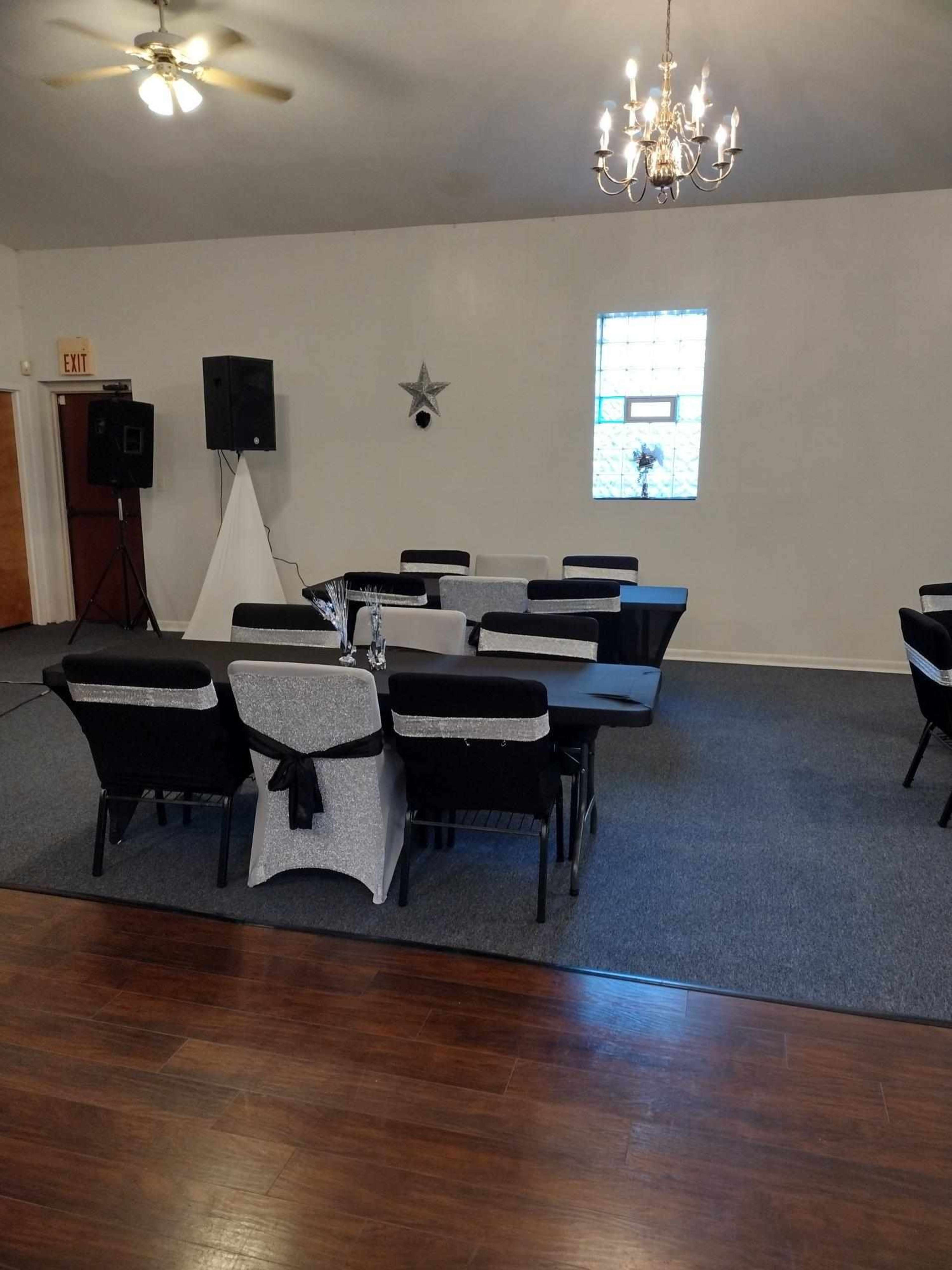 A spacious event room with black and silver table settings, a chandelier overhead, and a sound system in the corner.