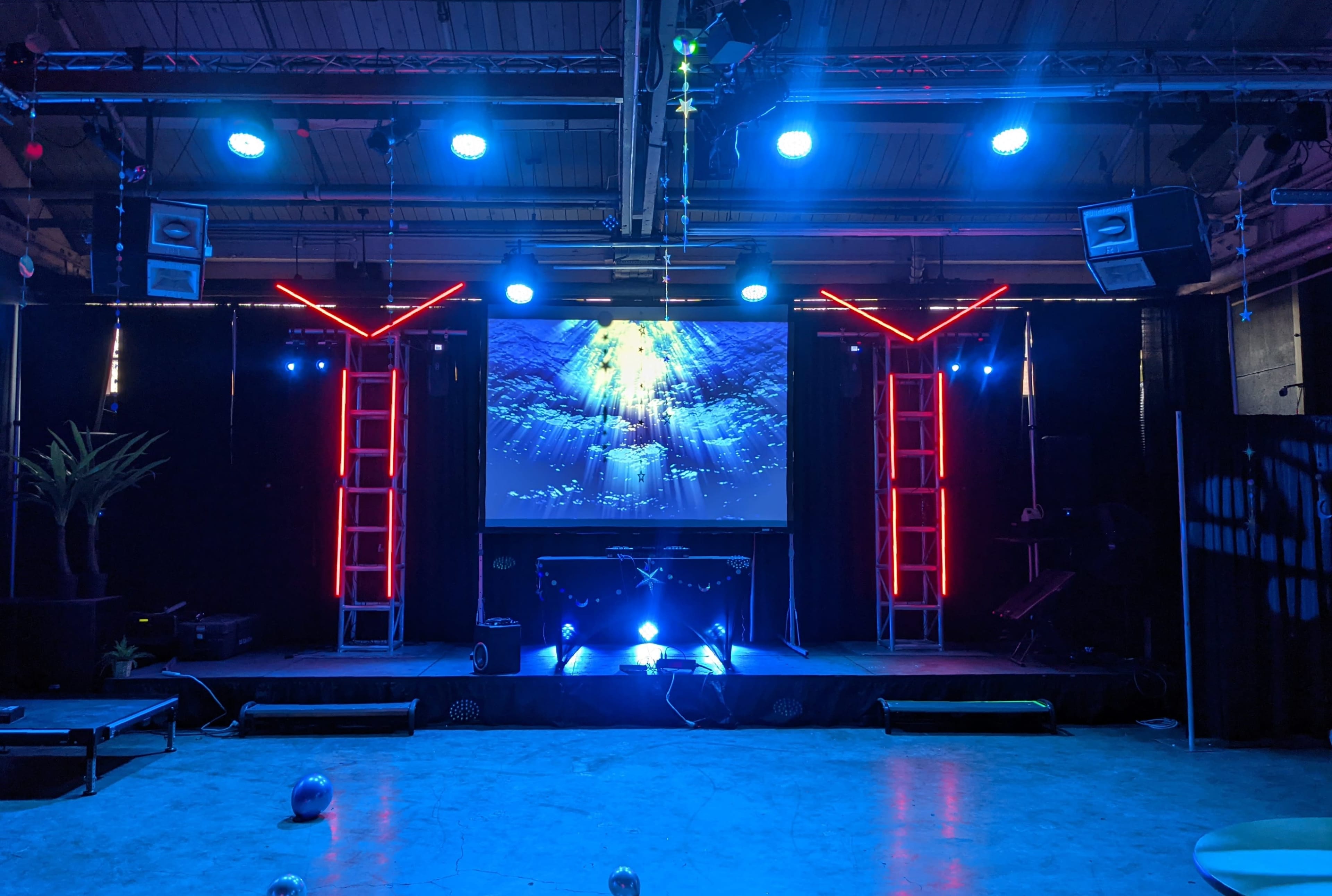 A stage setup with a large screen displaying an underwater scene, surrounded by illuminated frameworks and various lighting fixtures.