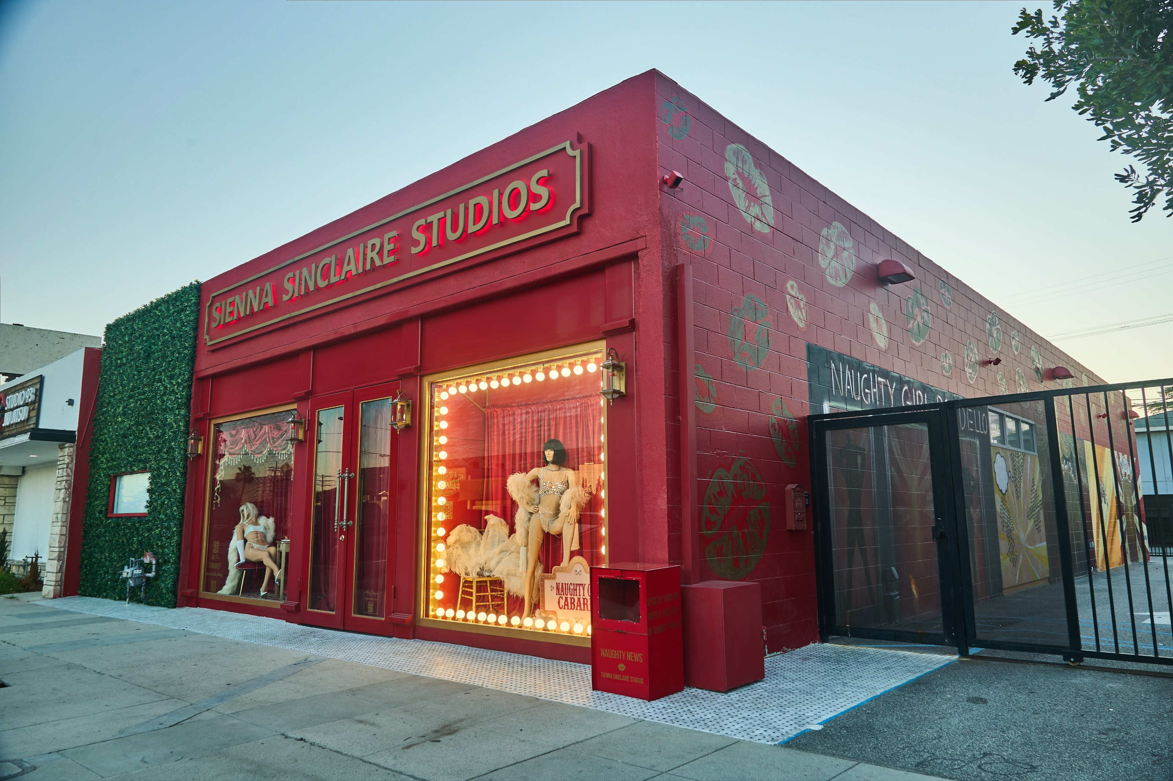 The image shows a brightly colored building with a red exterior and large windows displaying mannequins, labeled "Sienna Sinclaire Studios."