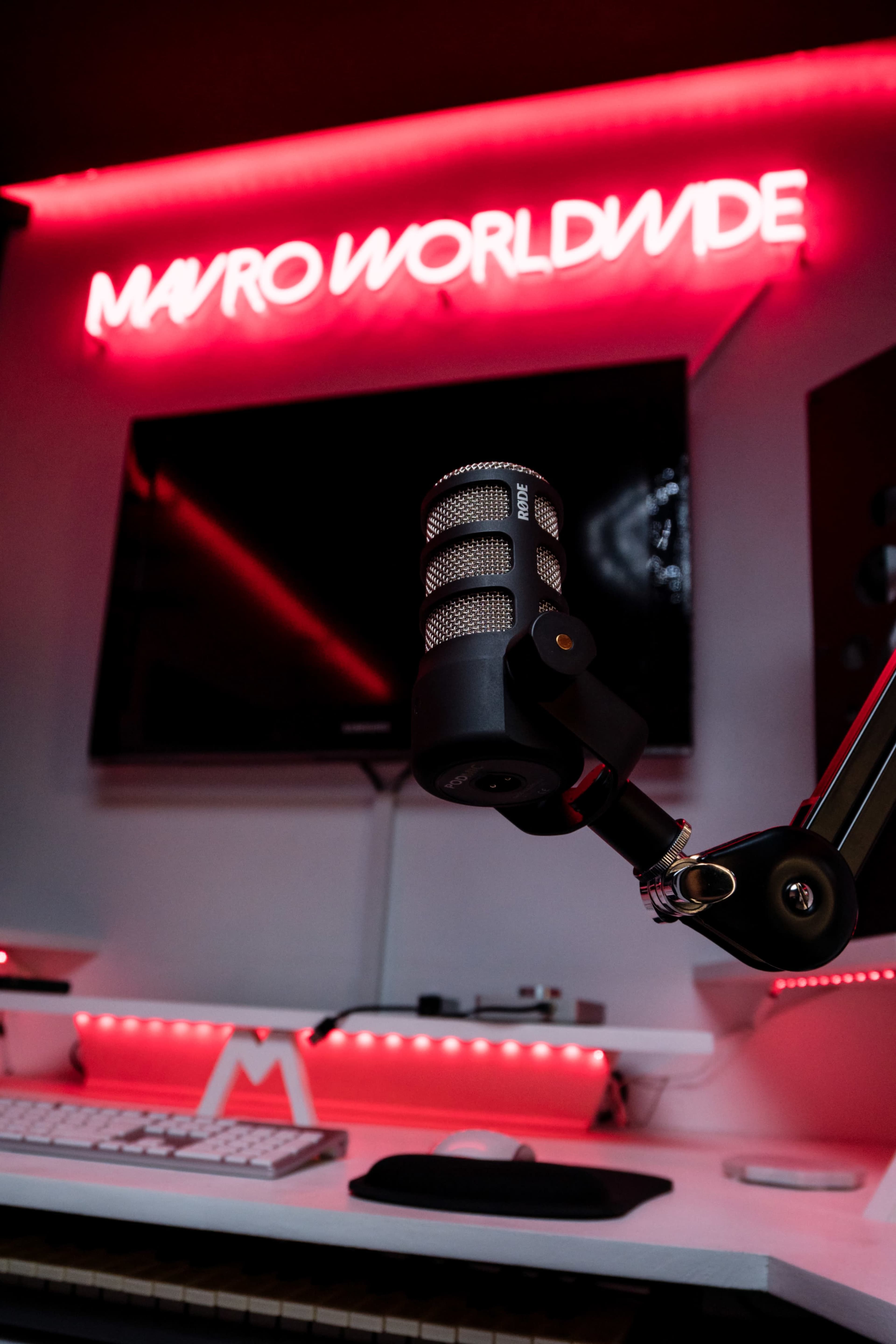 A studio setup features a microphone in the foreground with a glowing "MAYRO WORLDWIDE" sign in the background.