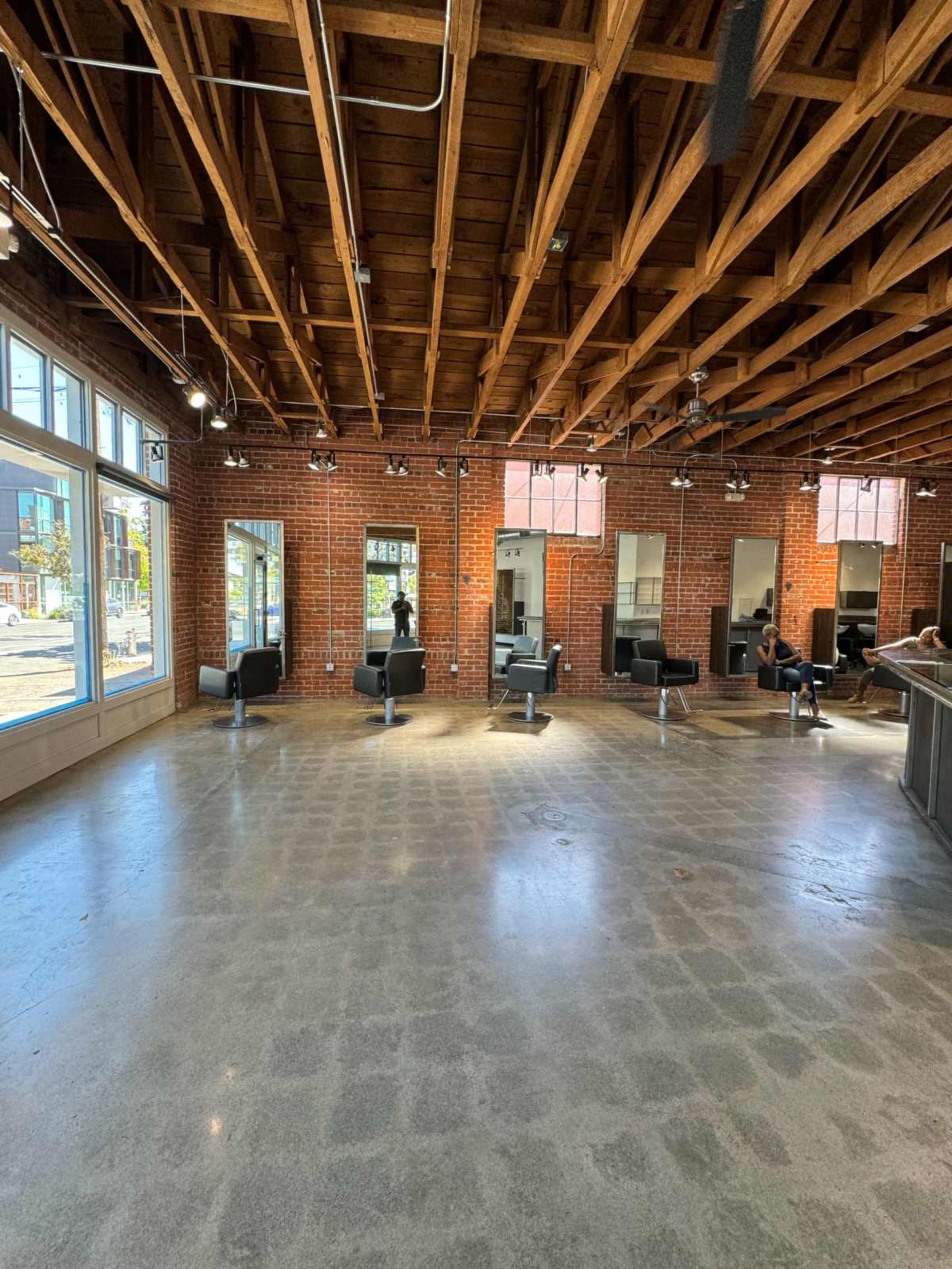 The image shows a spacious hair salon with exposed wooden beams, brick walls, and several styling stations lined along the mirrors.