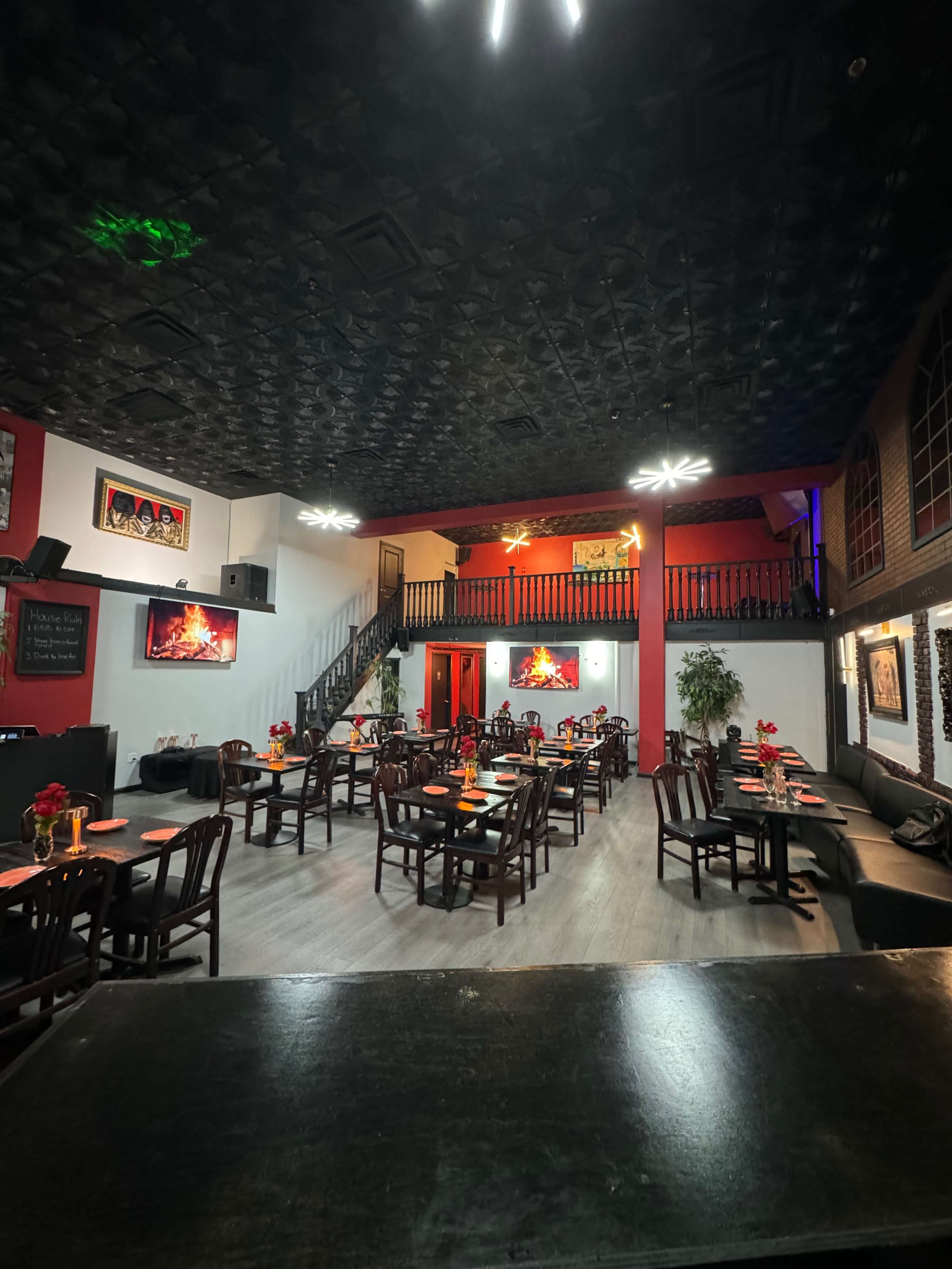 A spacious restaurant interior with tables set for dining, featuring a staircase and colorful lighting on the walls.