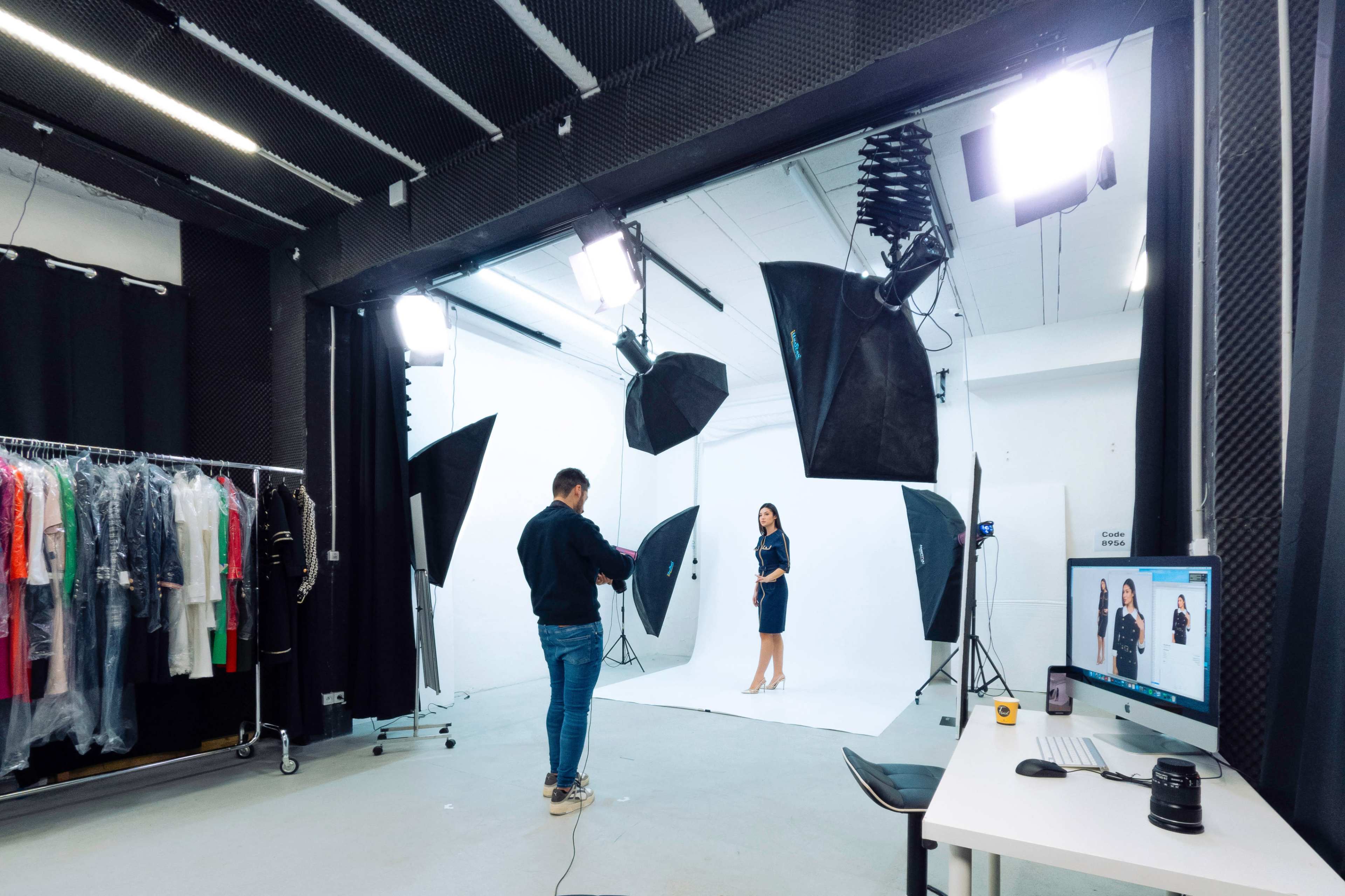 A photographer captures a model in a studio equipped with various lighting setups and a rack of clothing.
