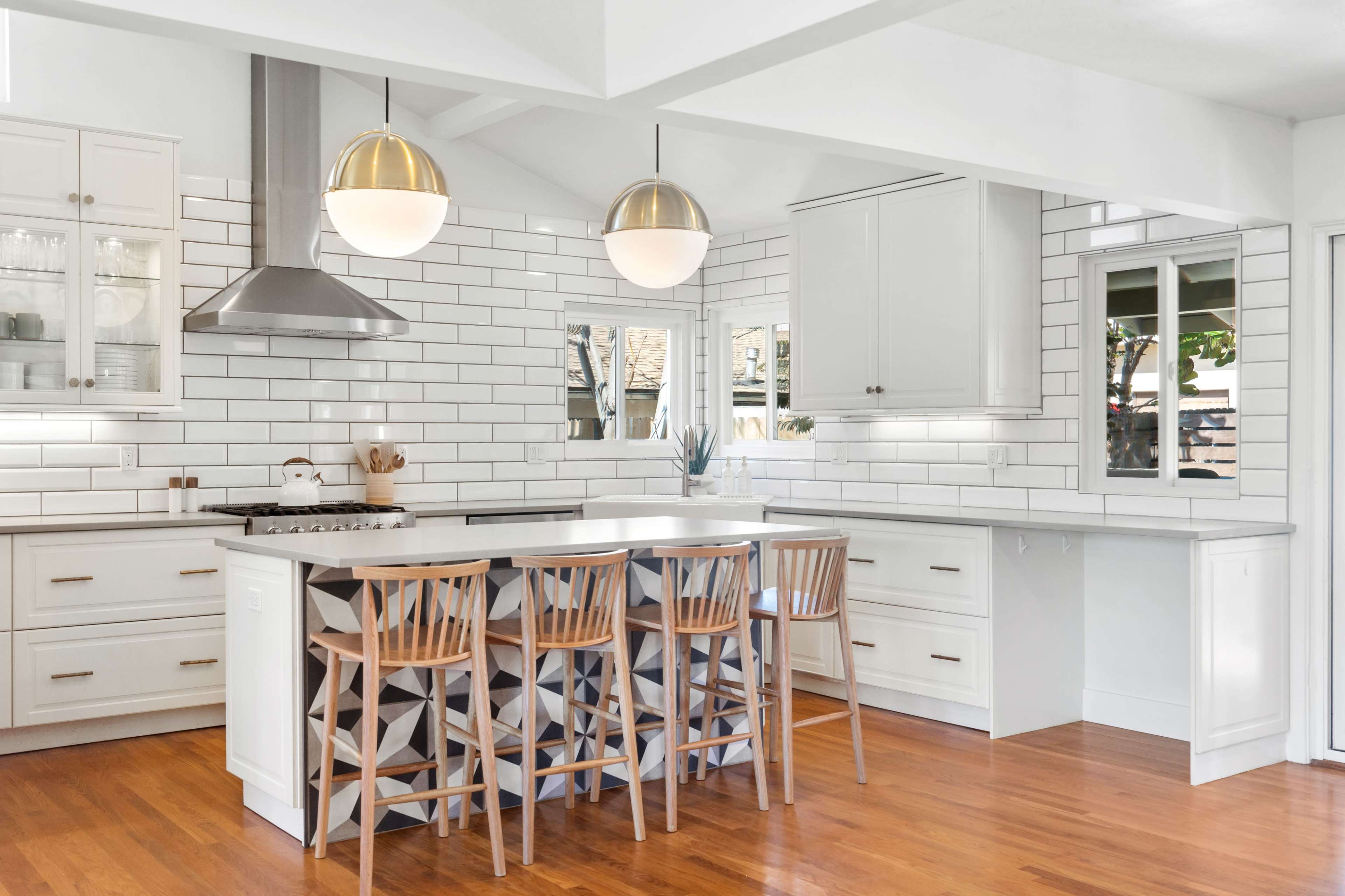 A modern kitchen featuring white cabinetry, a central island with wooden stools, and backsplash tiles arranged in a grid pattern.
