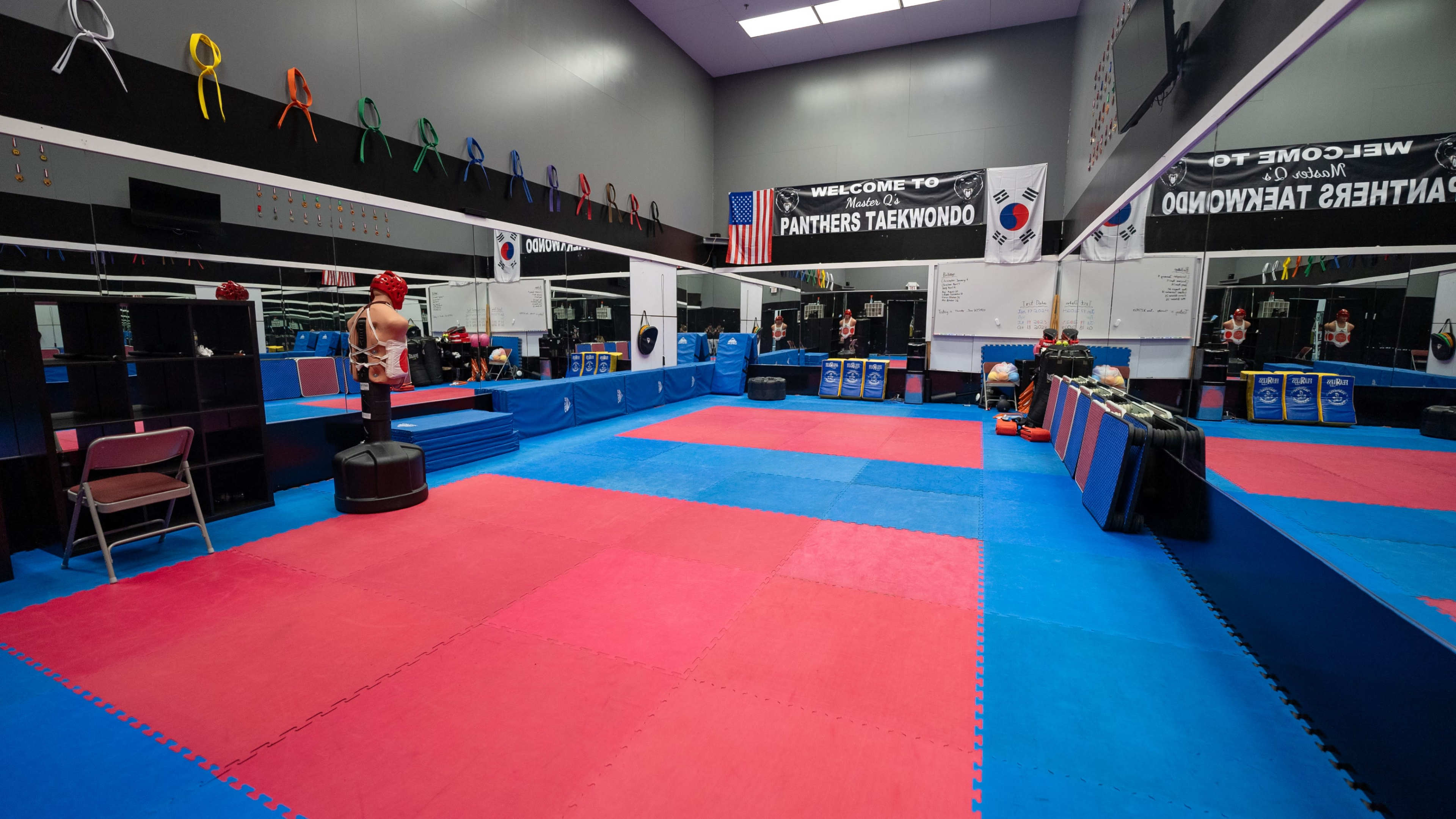 The image shows a taekwondo training studio with colorful mats, mirrors, and various training equipment arranged neatly along the walls.