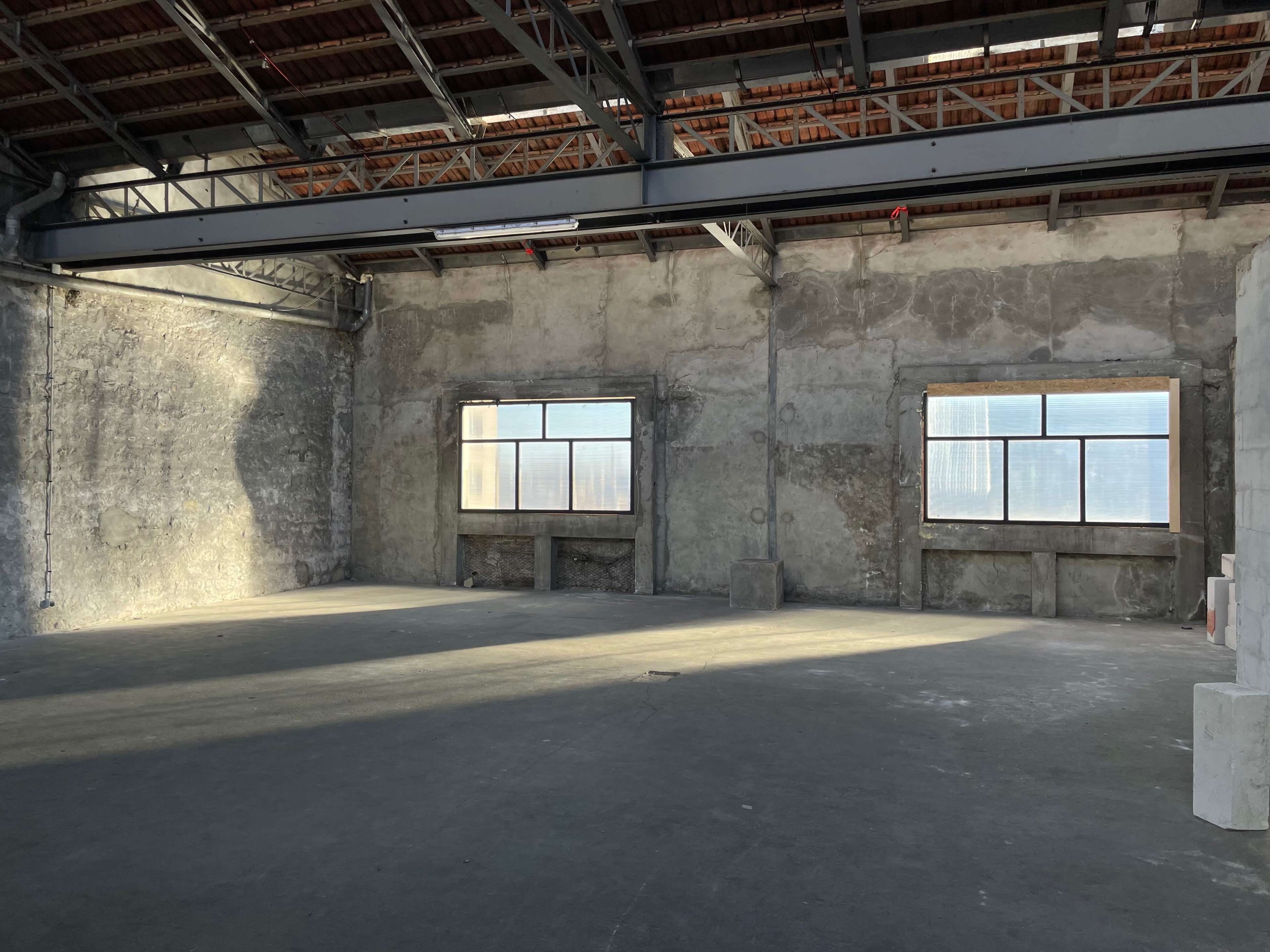An empty industrial space with concrete walls and large windows allowing natural light to enter.