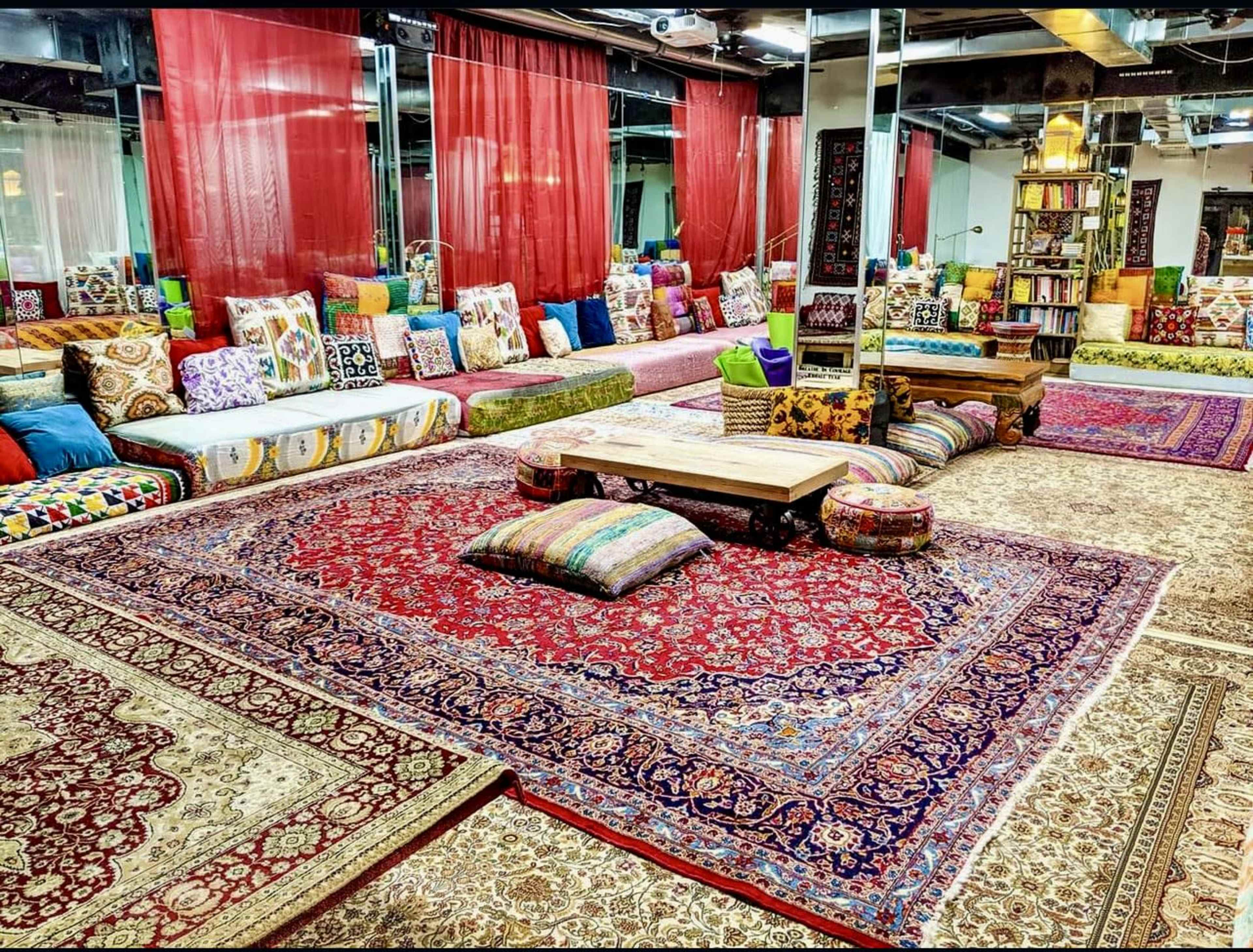 A cozy lounge area with colorful cushions and rugs, arranged around a low wooden table in a warmly lit space.