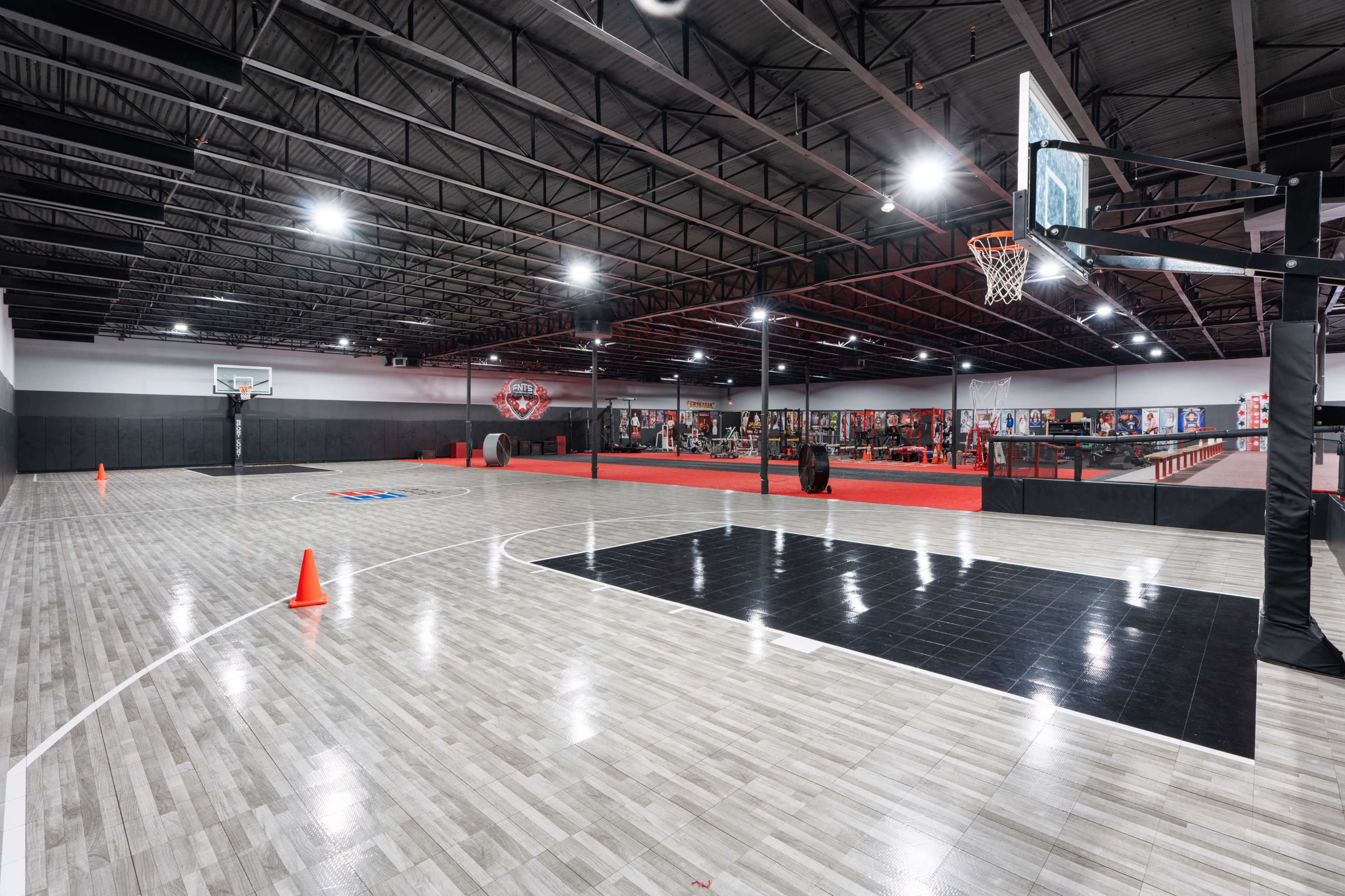 A spacious indoor basketball court with marked lines, basketball hoops at either end, and orange cones placed around the perimeter.