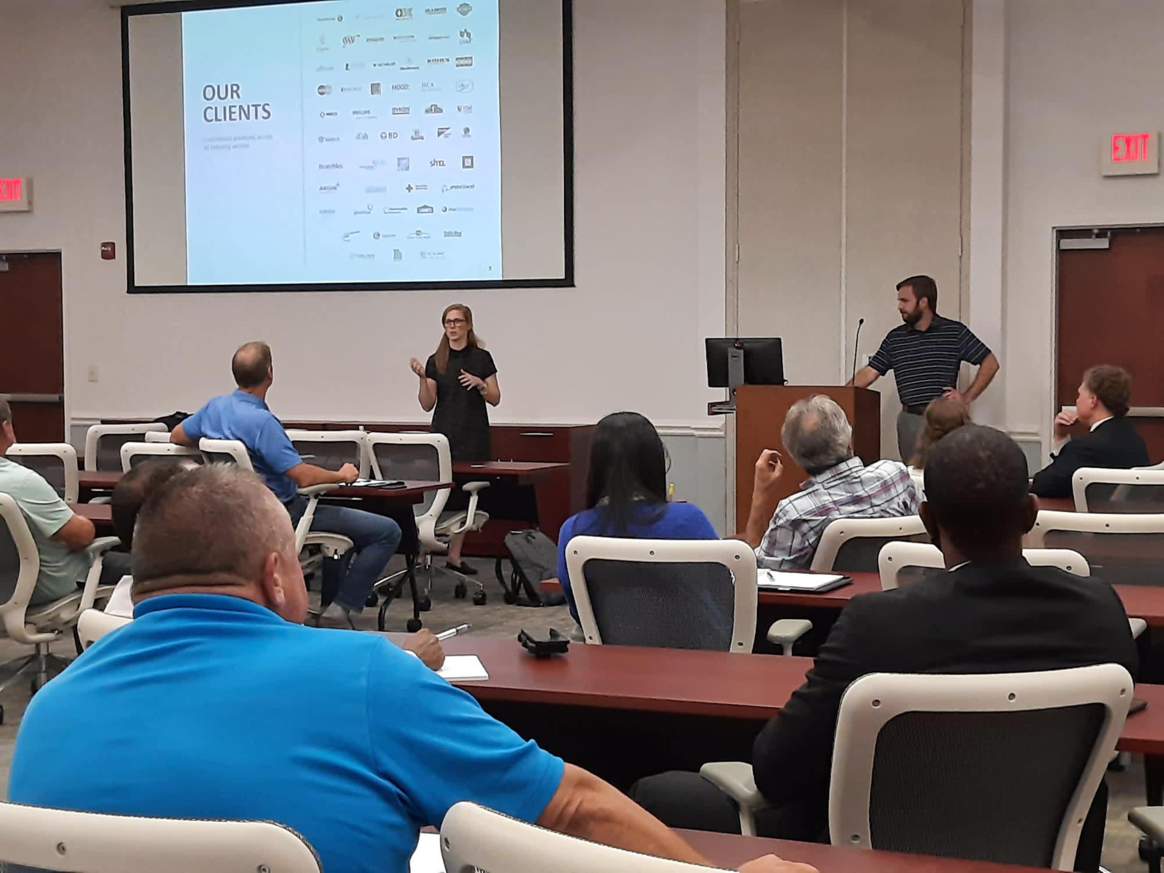 A presenter shares information about clients in a conference room while an audience listens attentively.