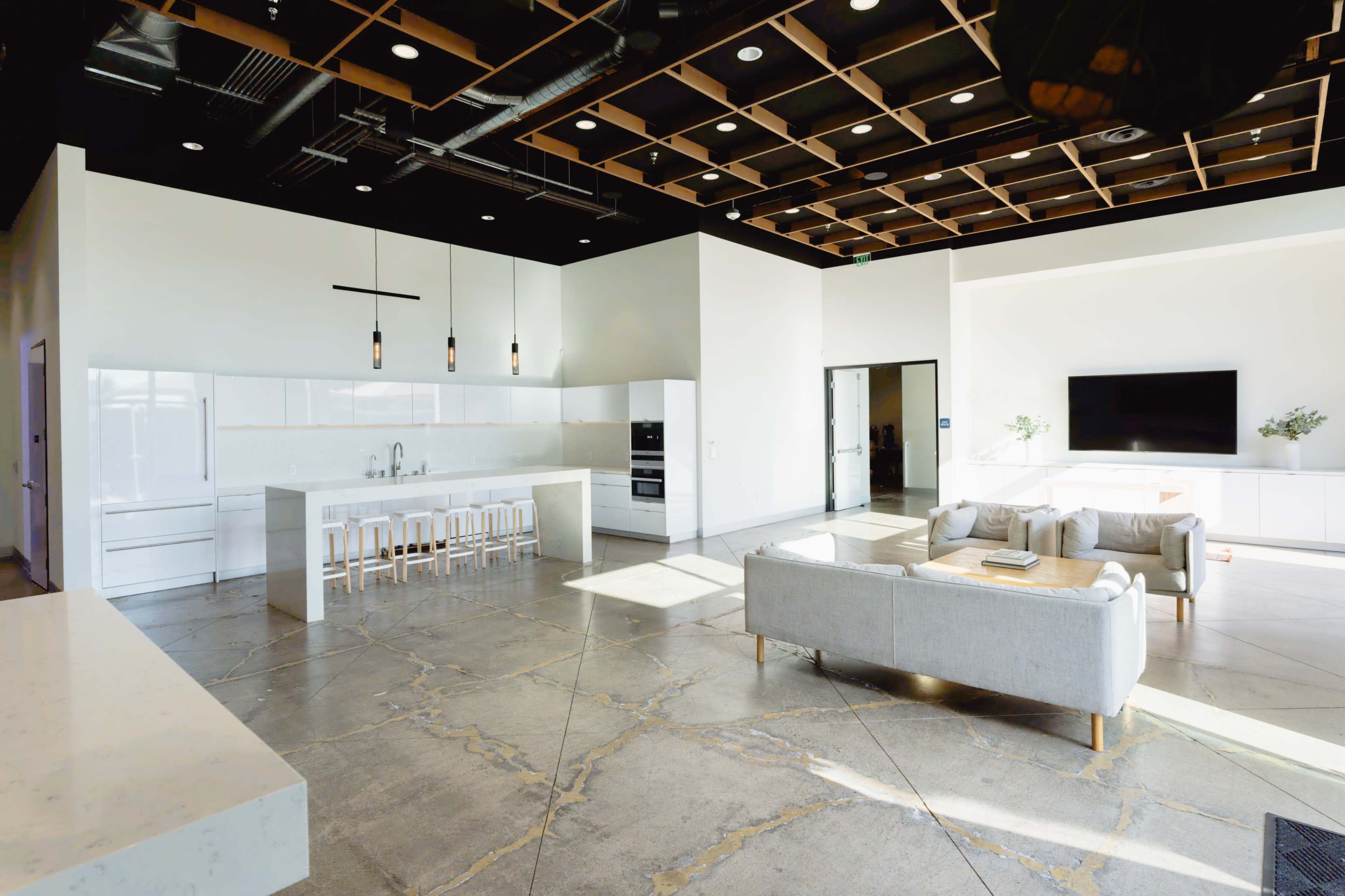 The image shows a modern open-concept kitchen and living area with a large island, bar stools, and a comfortable seating arrangement.