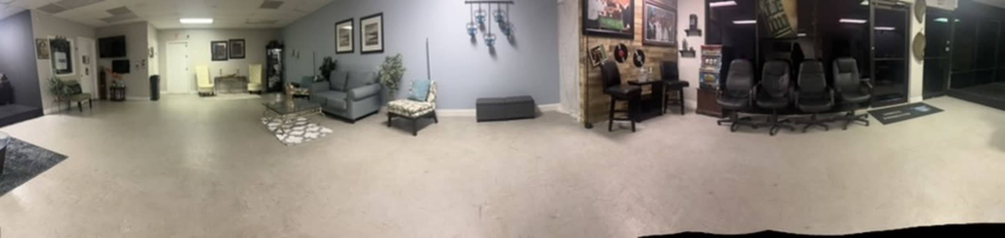 The image shows a spacious lobby area with seating arrangements, decorative plants, and framed artwork on the walls.