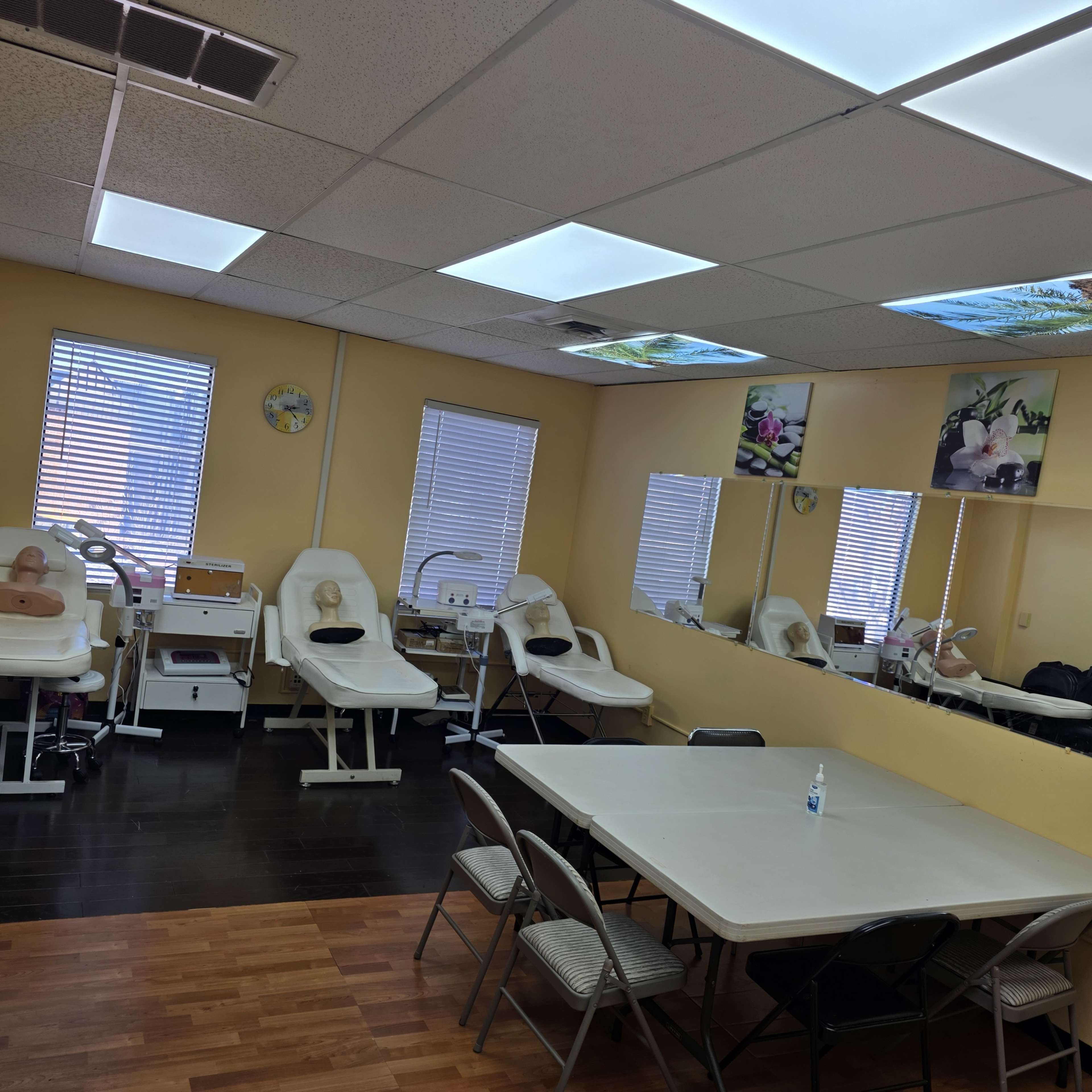 The image shows a training room with multiple massage tables, a mirrored wall, and a table with chairs in a well-lit area.