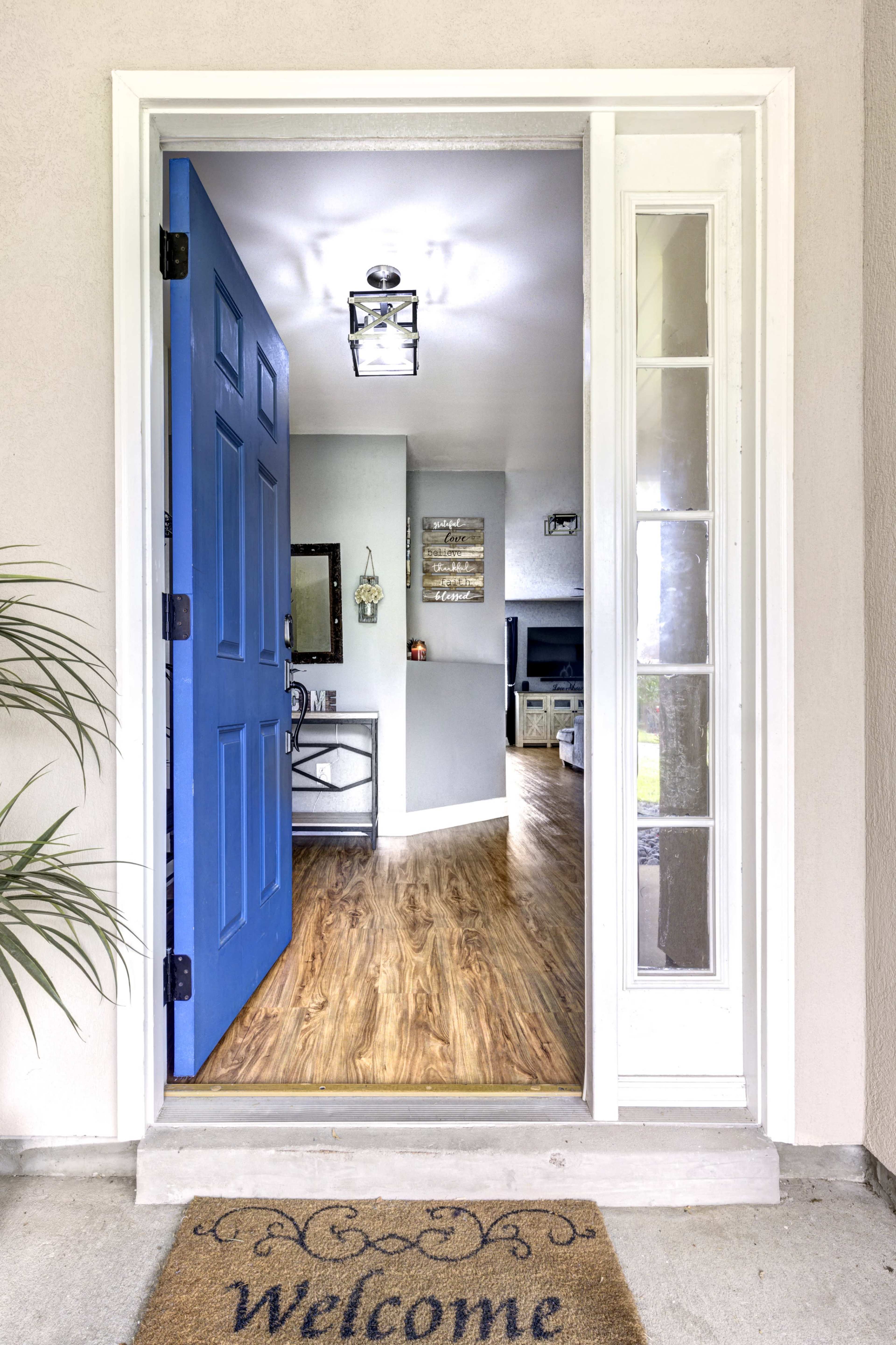 A blue front door stands open, revealing a hallway with wooden flooring and furnishings visible inside.