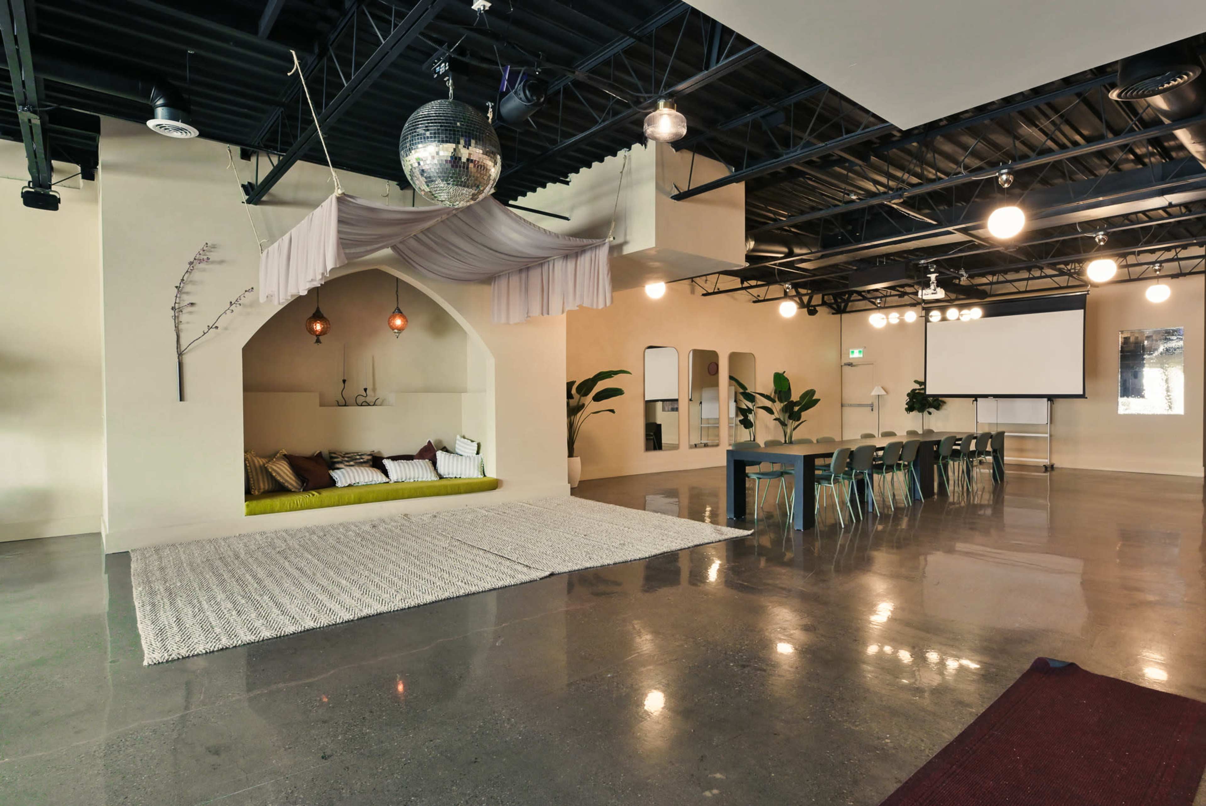 The image shows a modern, spacious interior featuring a lounge area with a green seating section and a large table surrounded by chairs.