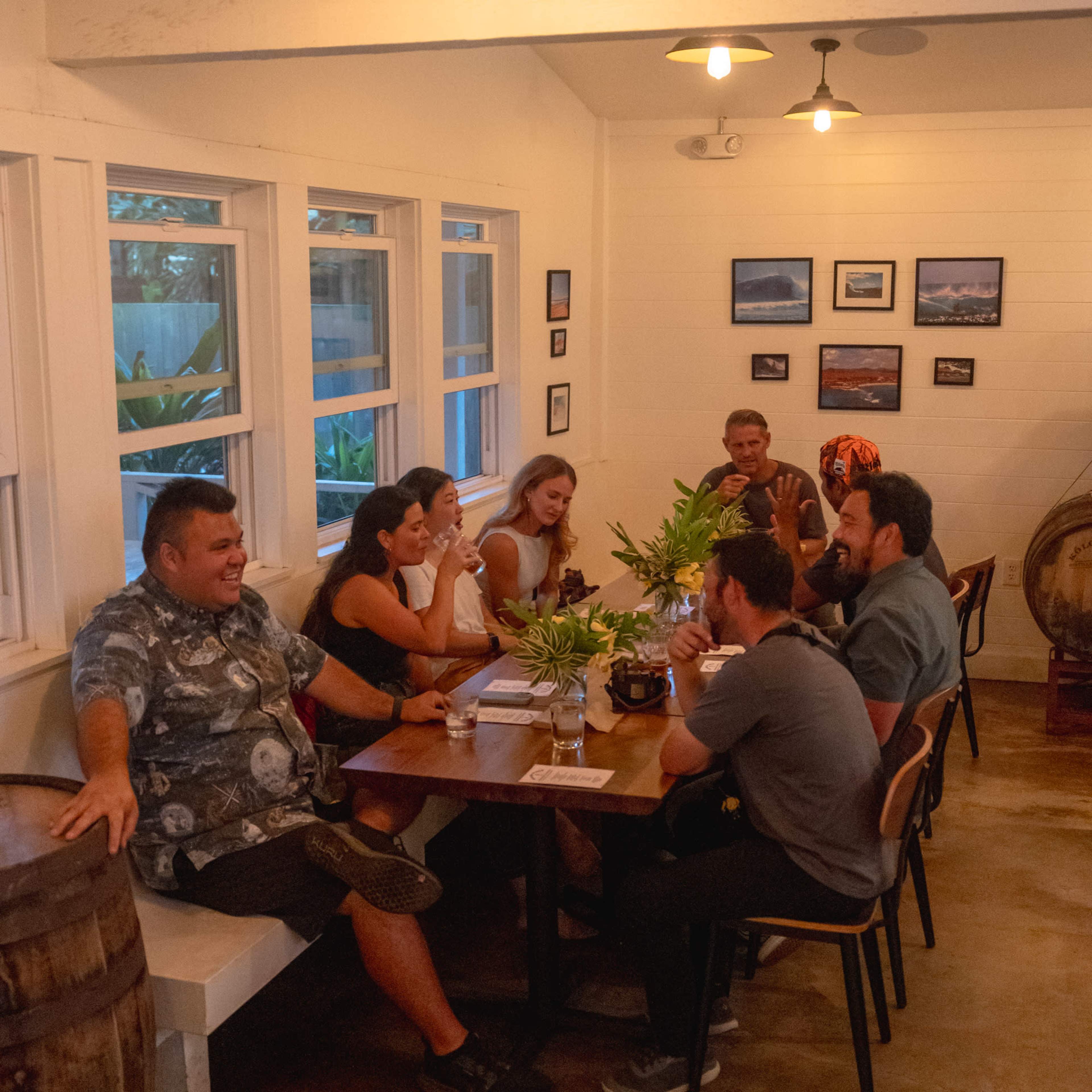 A group of six people sits around a wooden table in a well-lit room decorated with wall art, engaged in conversation.