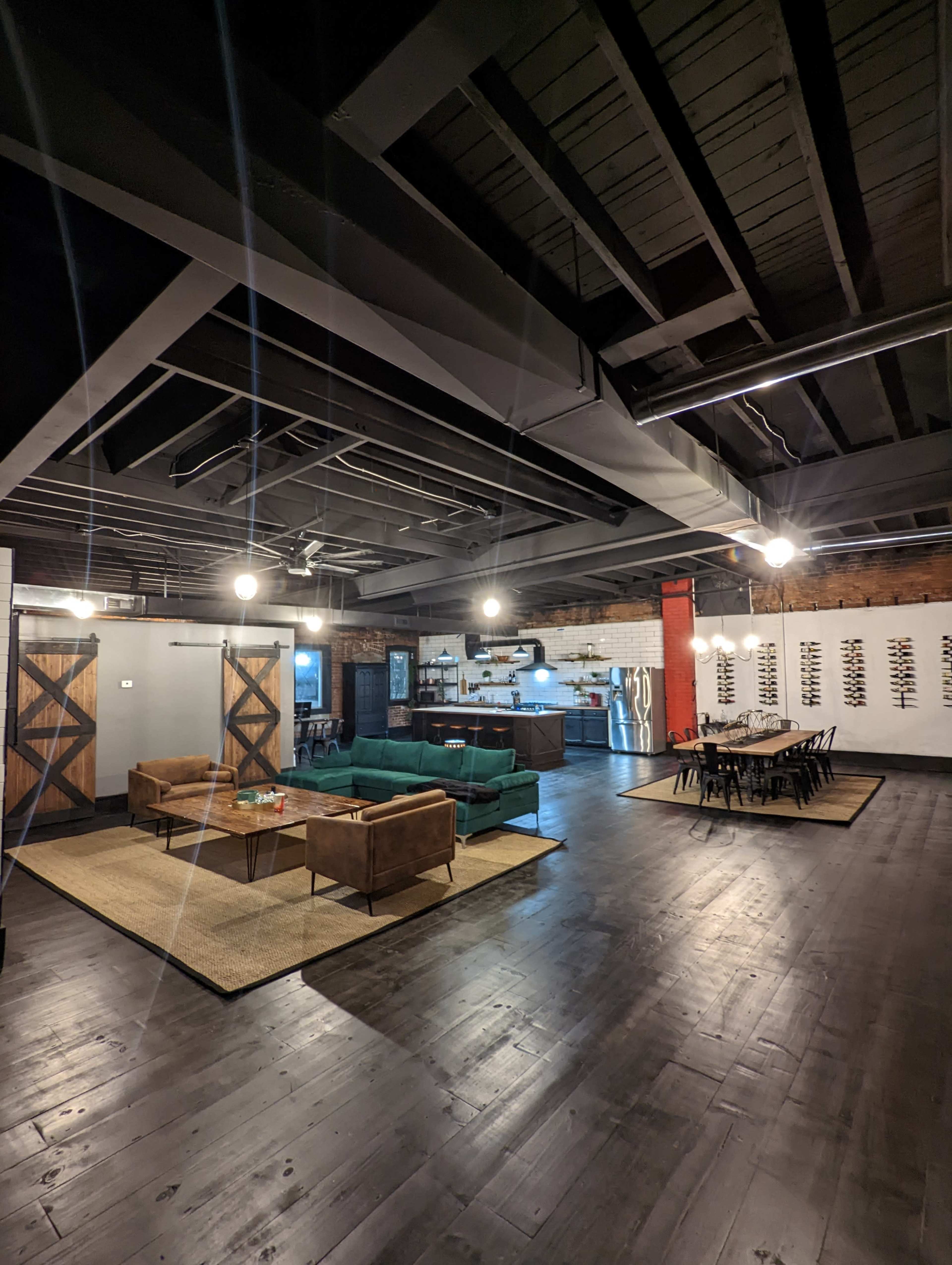 A spacious, modern interior with dark wooden floors, a green sofa, brown couches, a dining table, and a kitchen area in the background.