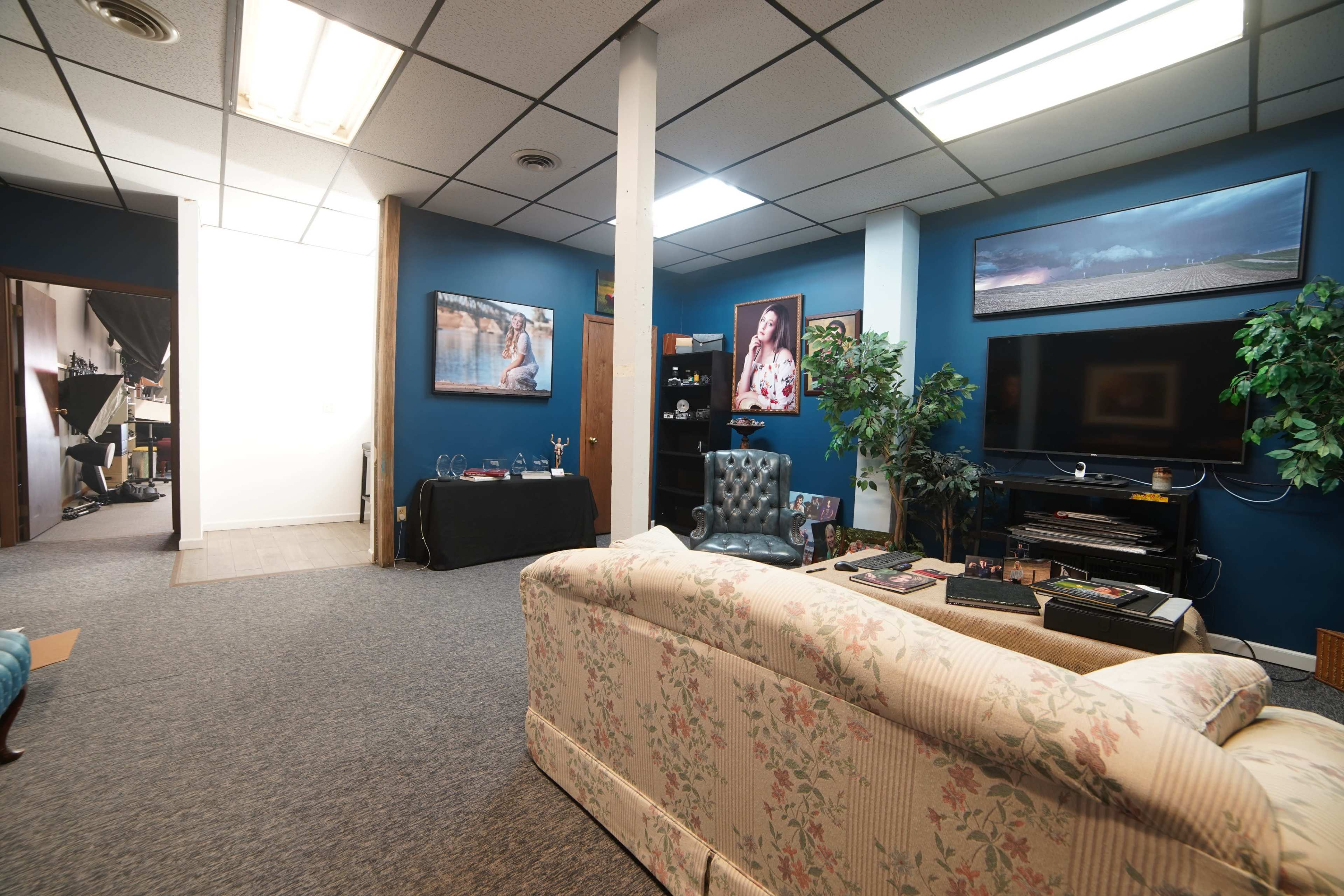 The image shows a cozy office space with blue walls, a patterned couch, a television, and various decorations on shelves and walls.