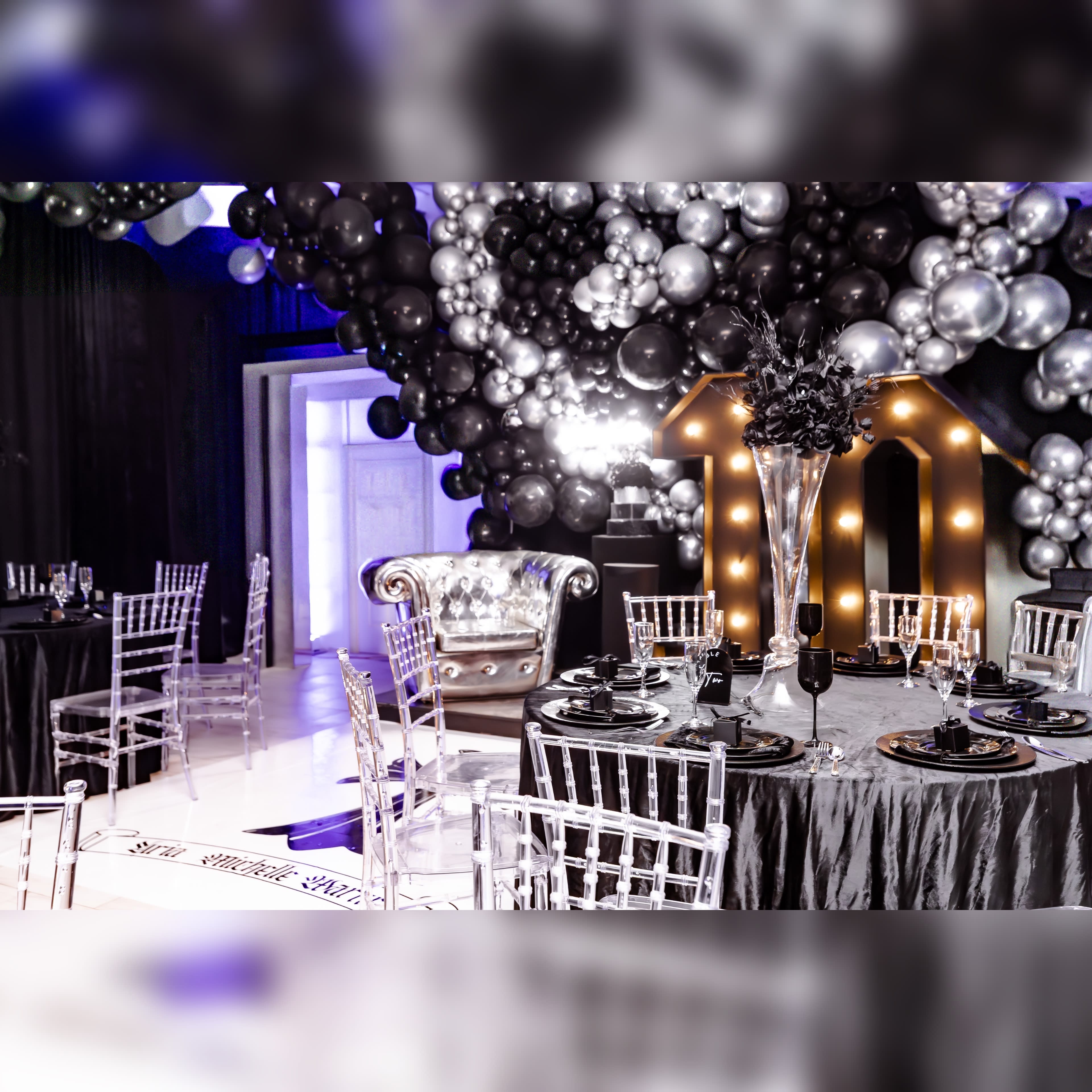 The scene features a stylish party setup with black and silver balloons overhead, elegant tables with dark tablecloths, and a large illuminated "10" decoration.