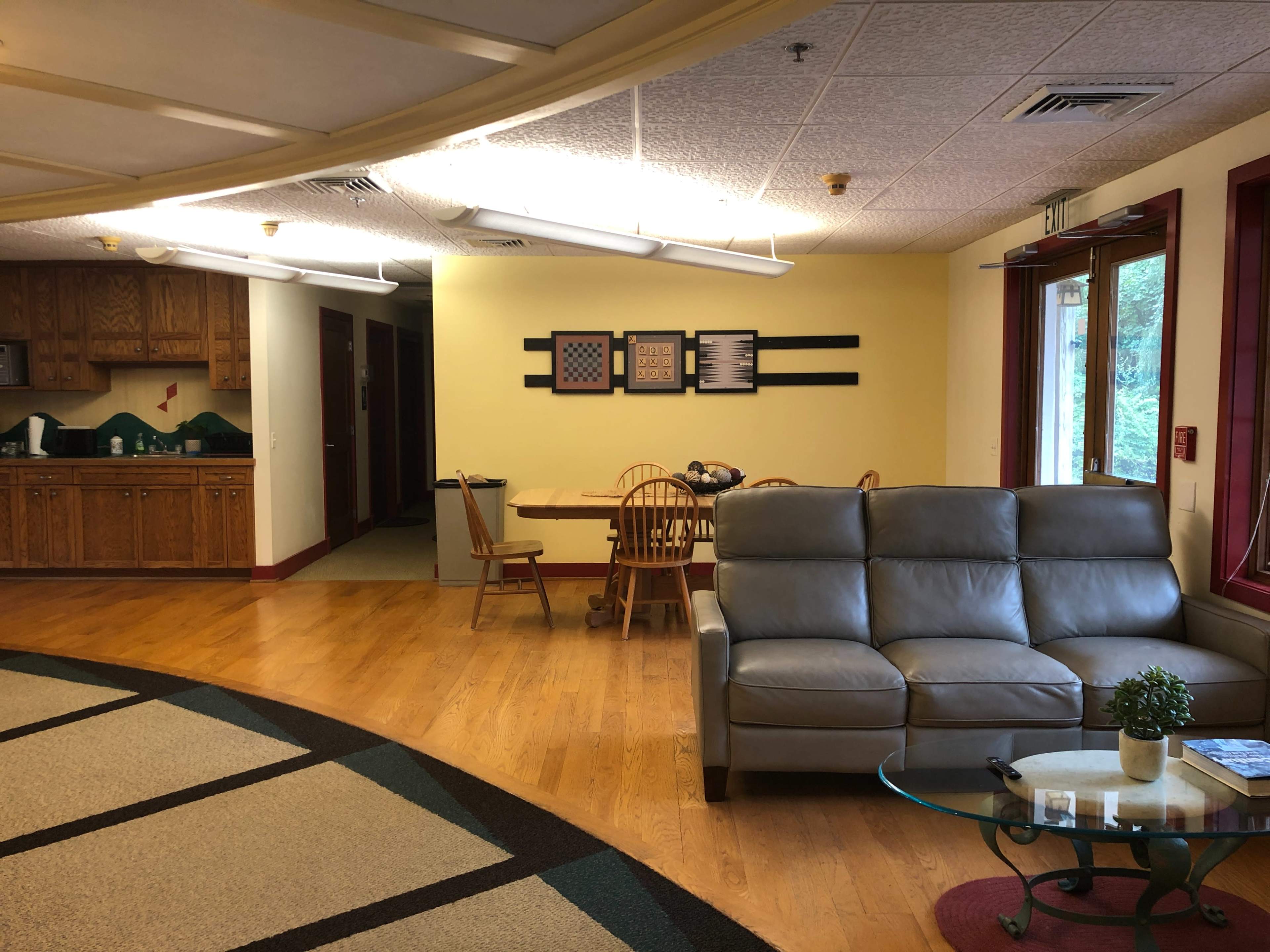 A communal living area with a light-colored kitchen, dining table, and a gray sofa.
