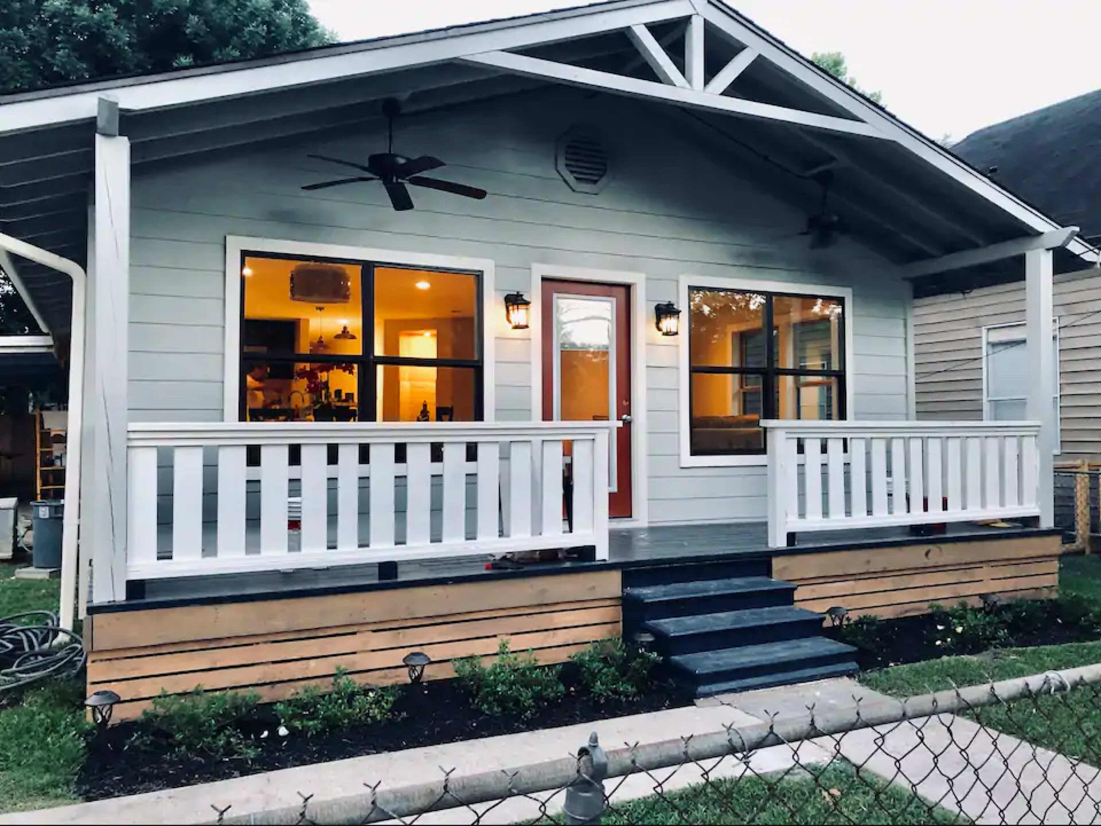 A renovated one-story house with a spacious front porch, two ceiling fans, and large windows, surrounded by a well-maintained yard.