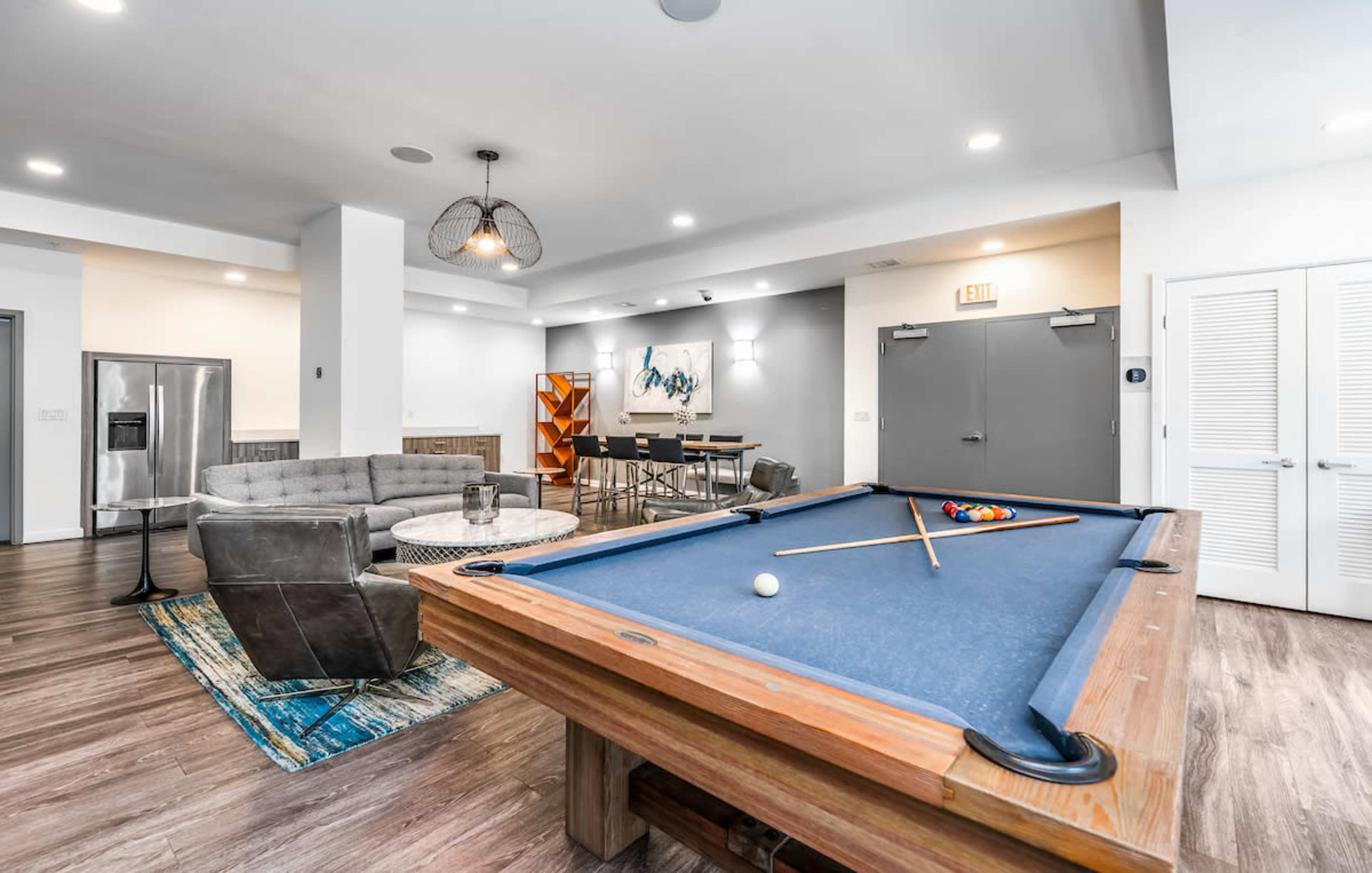 A modern game room featuring a billiard table, a seating area with a gray couch, and a dining table in the background.
