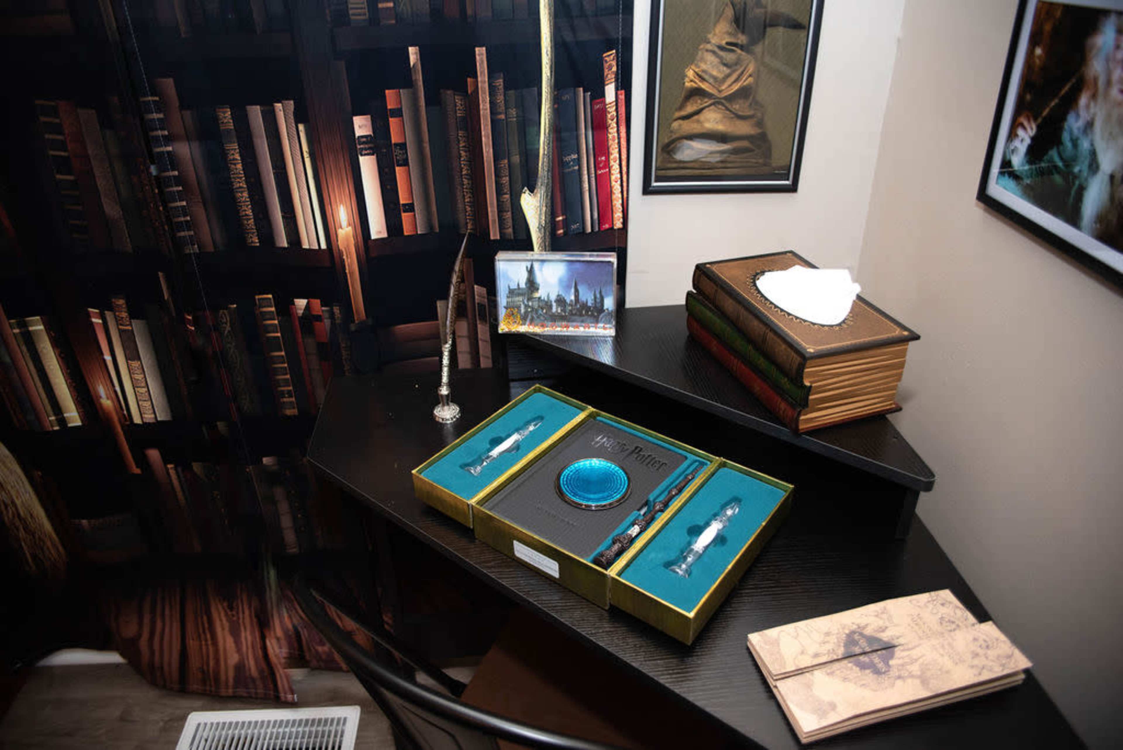 A dark wooden desk with a collection of decorative items, including a box set of "Harry Potter" memorabilia, quills, and a framed photo, all set against a backdrop of bookshelves filled with books.