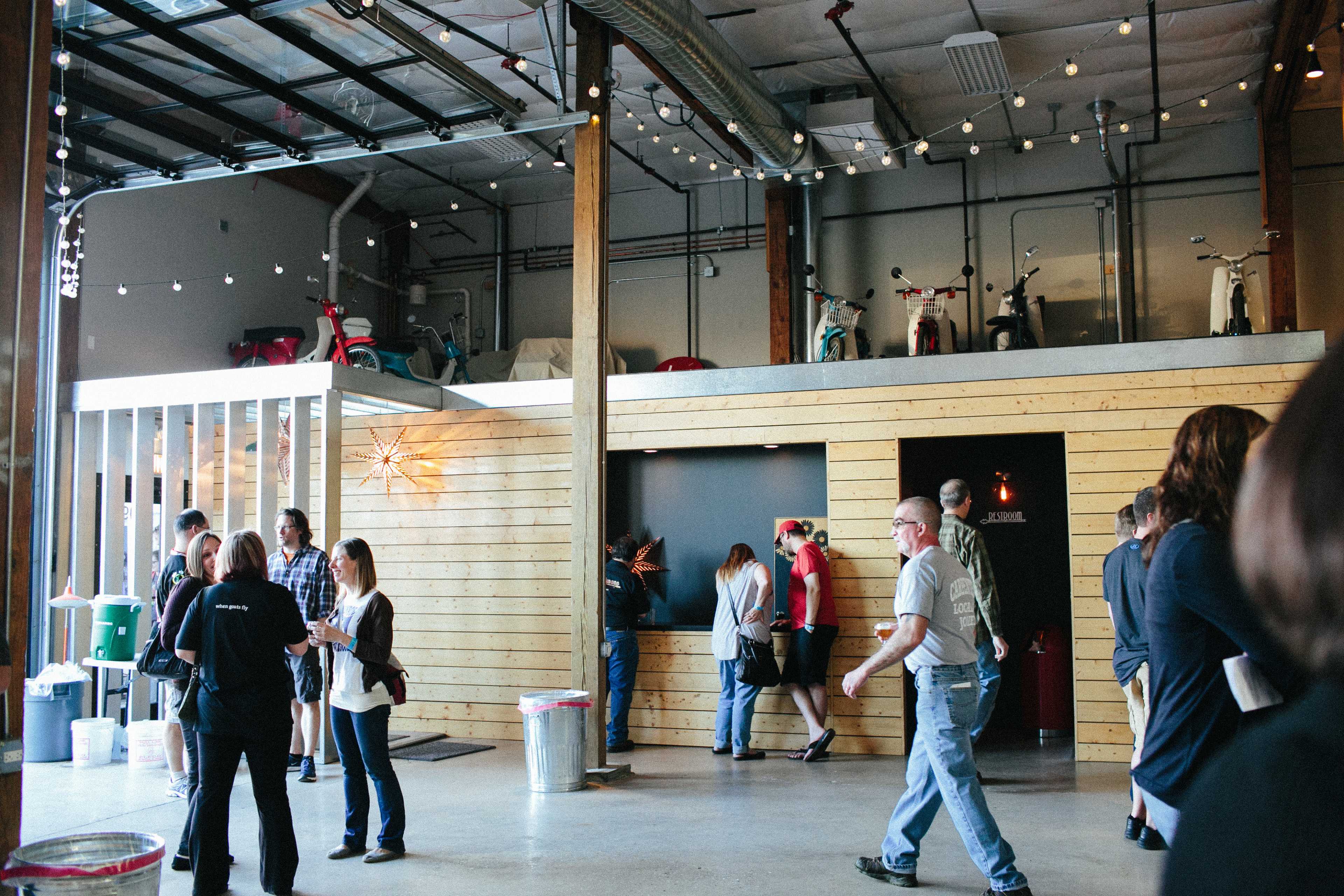 A modern indoor space features people engaging with one another, wooden walls, and scooters displayed on a platform above.