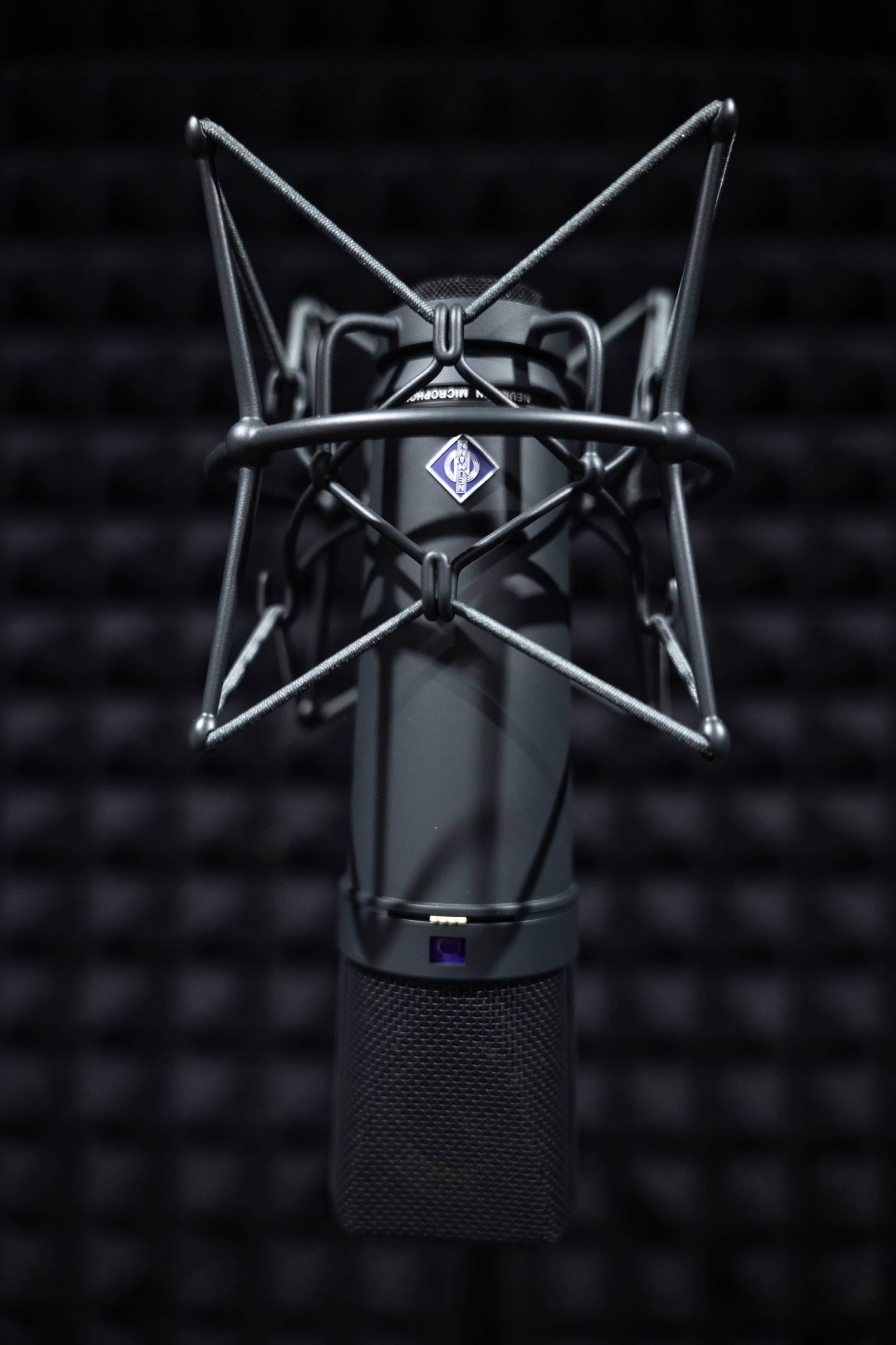 A close-up of a black microphone with a shock mount against a textured background.