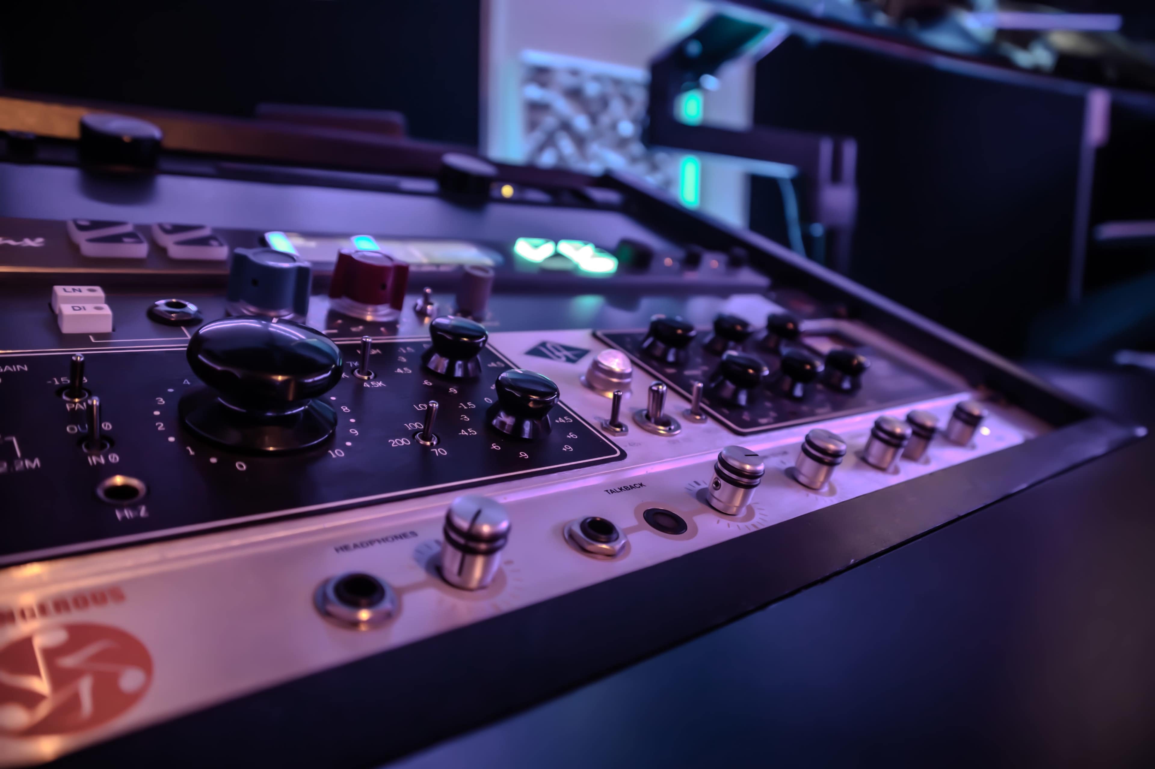 The image shows a close-up view of a sound mixing console with various knobs and buttons in a dimly lit environment.
