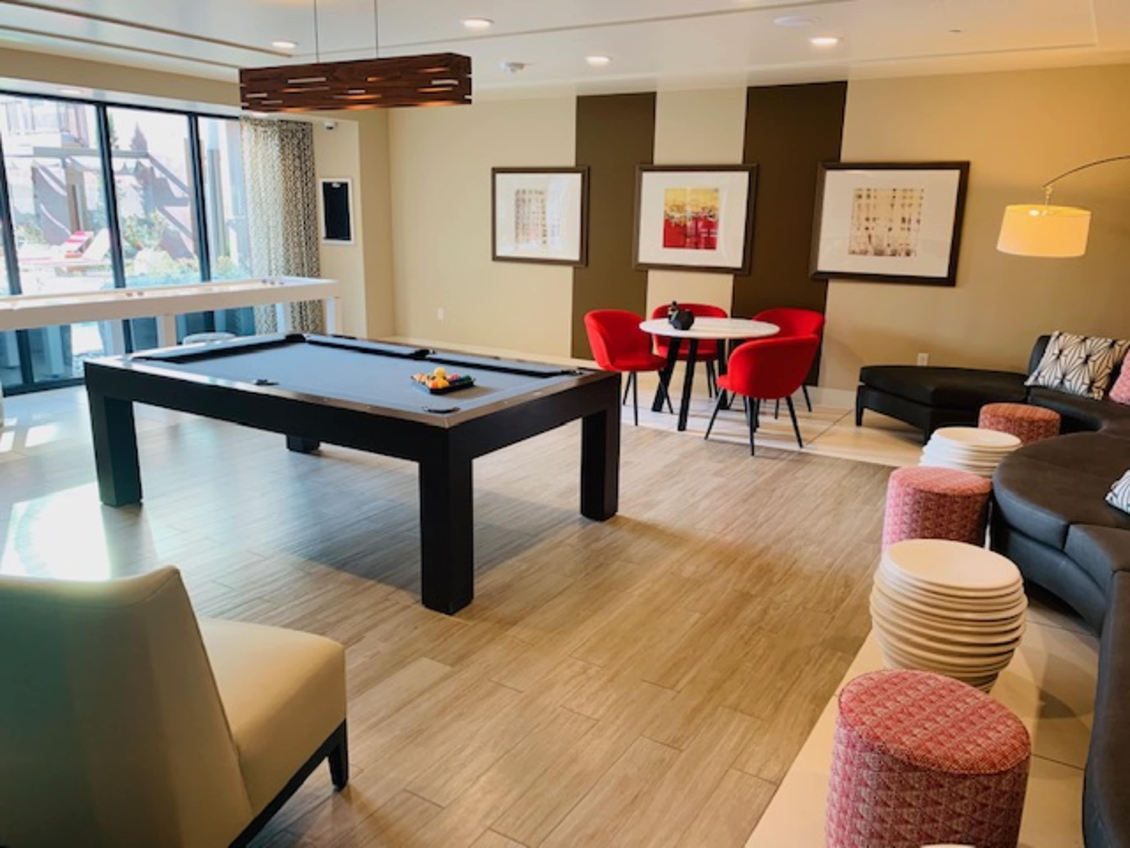 A modern lounge area featuring a pool table, a round dining table with red chairs, and a sectional sofa.