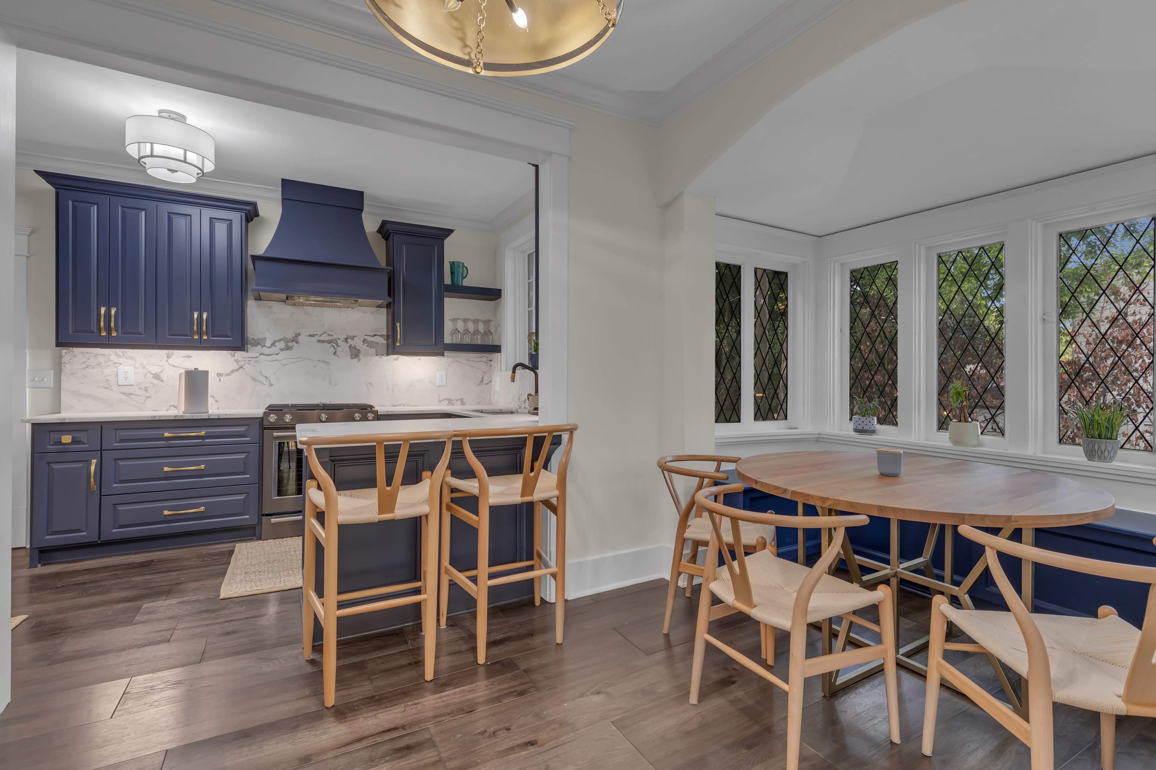 A modern kitchen features navy blue cabinetry, a marble backsplash, and a dining area with a round wooden table and chairs.