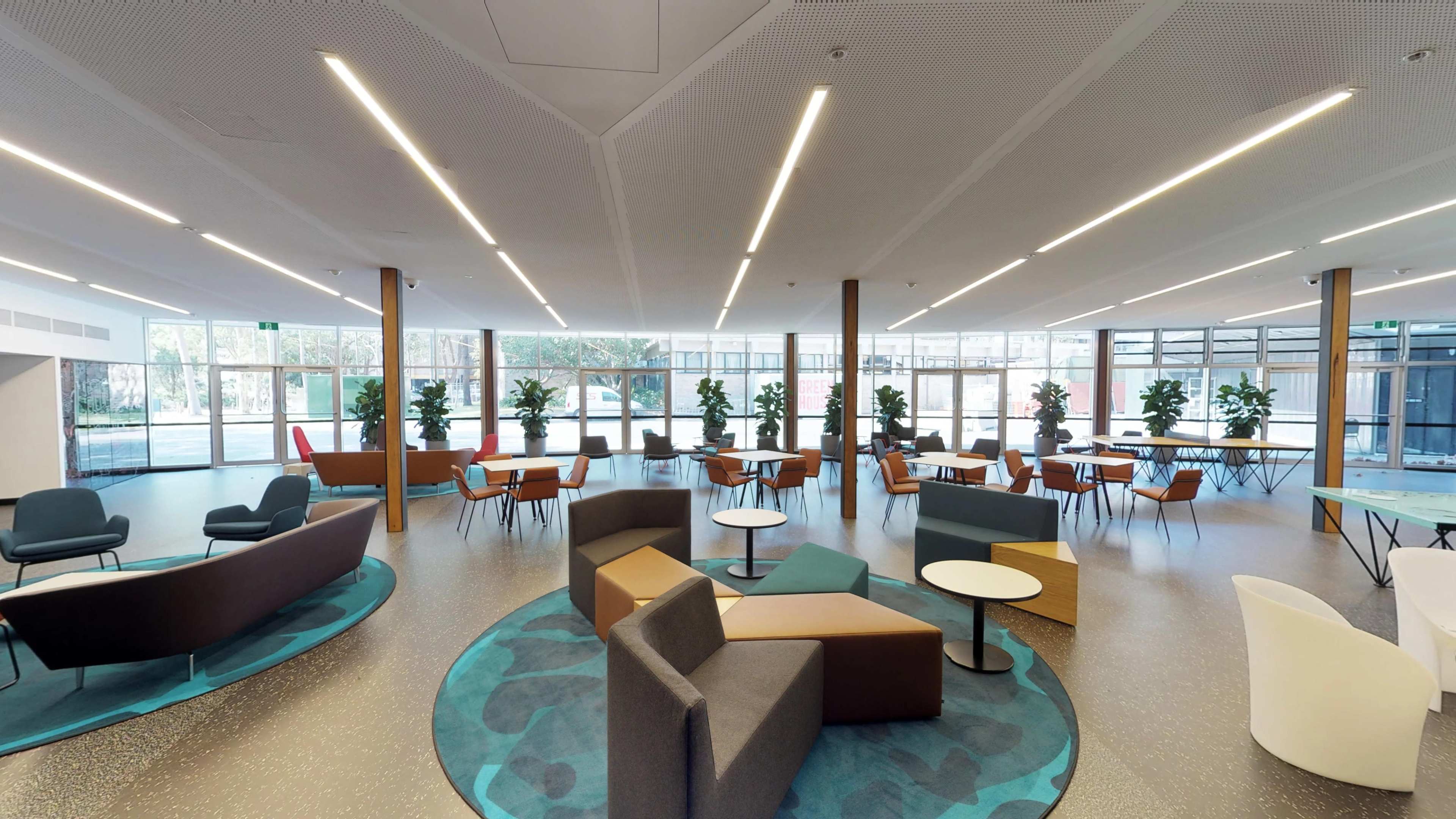 A modern indoor lounge area with various seating arrangements and large windows allowing natural light to enter.