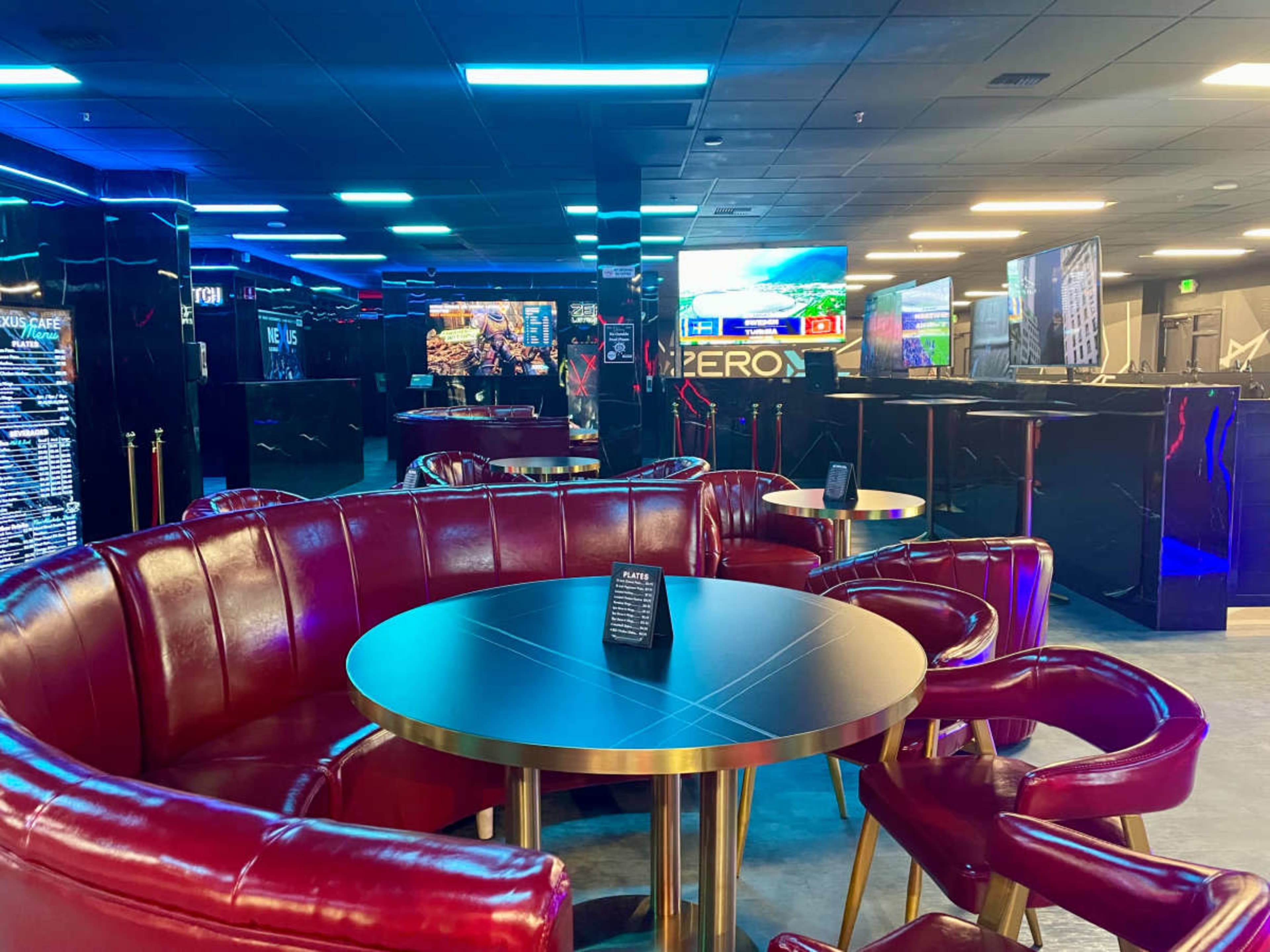 The image shows a modern lounge area with red leather seating, black accents, and several screens displaying information or entertainment.